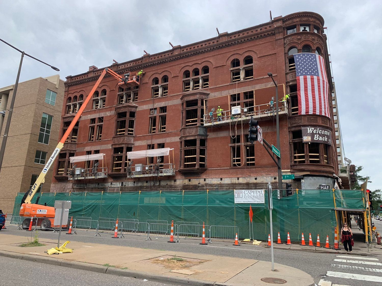 A large brick building is being remodeled with an american flag on the side.