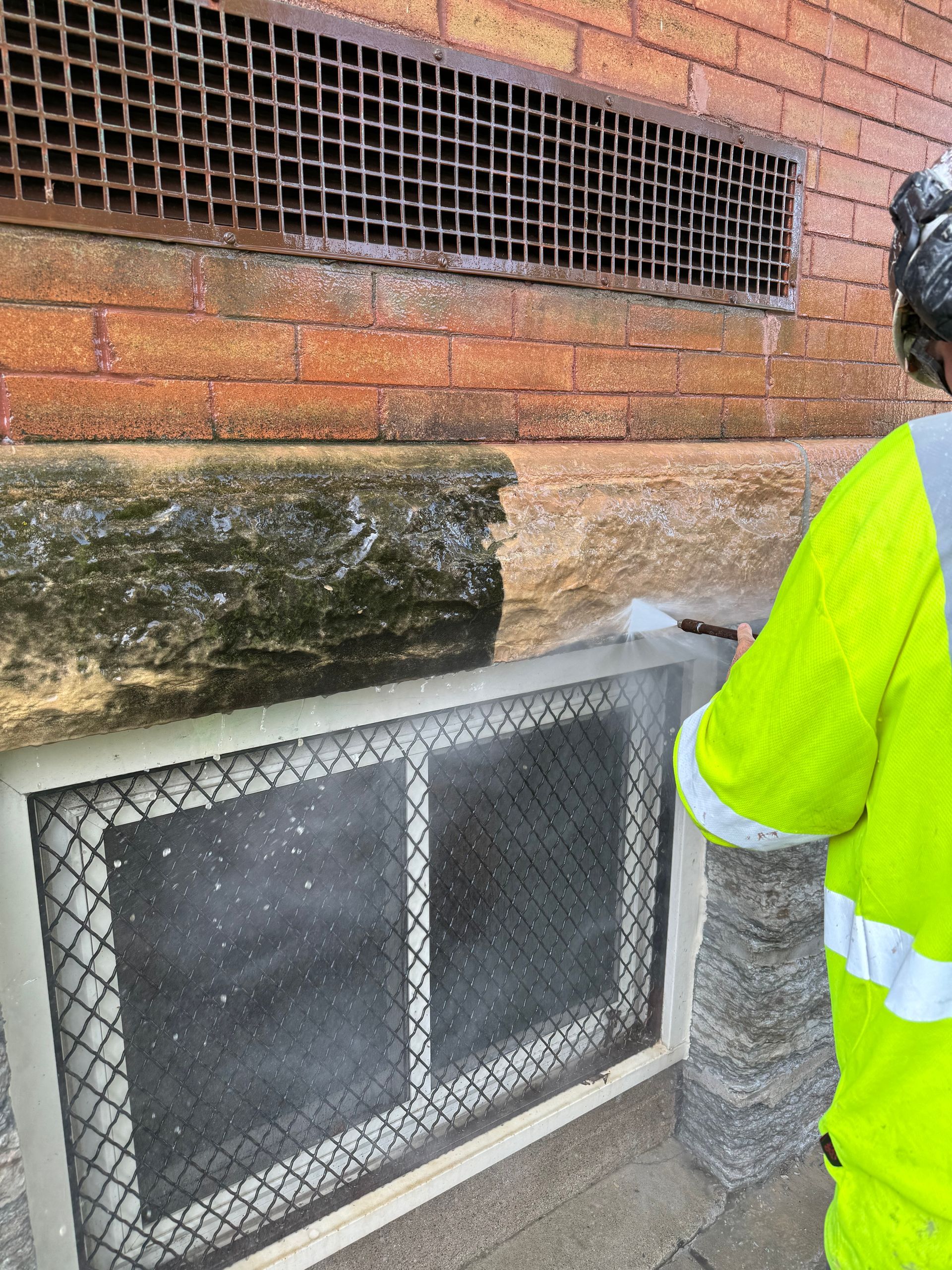 A man in a yellow jacket is cleaning a window on a brick wall.