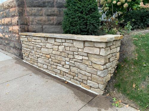 A stone wall with a planter in the middle of it next to a sidewalk.