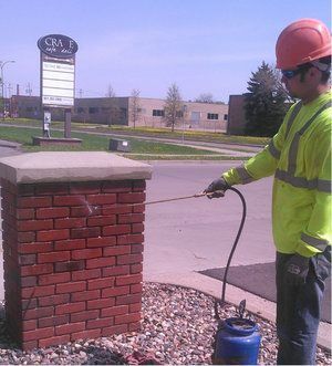A man wearing a hard hat is spraying a brick column with a hose