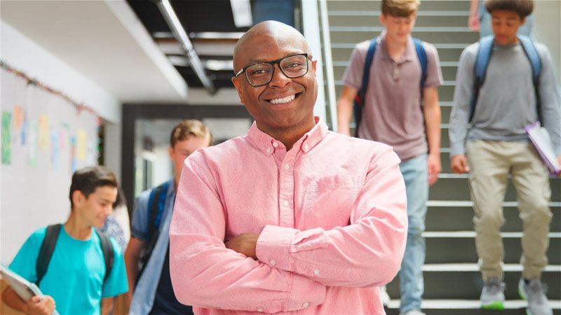 A man in a pink shirt is standing in a hallway with his arms crossed. Top Questions to Ask College Recruiters to Gaining Valuable Insights at College Fairs