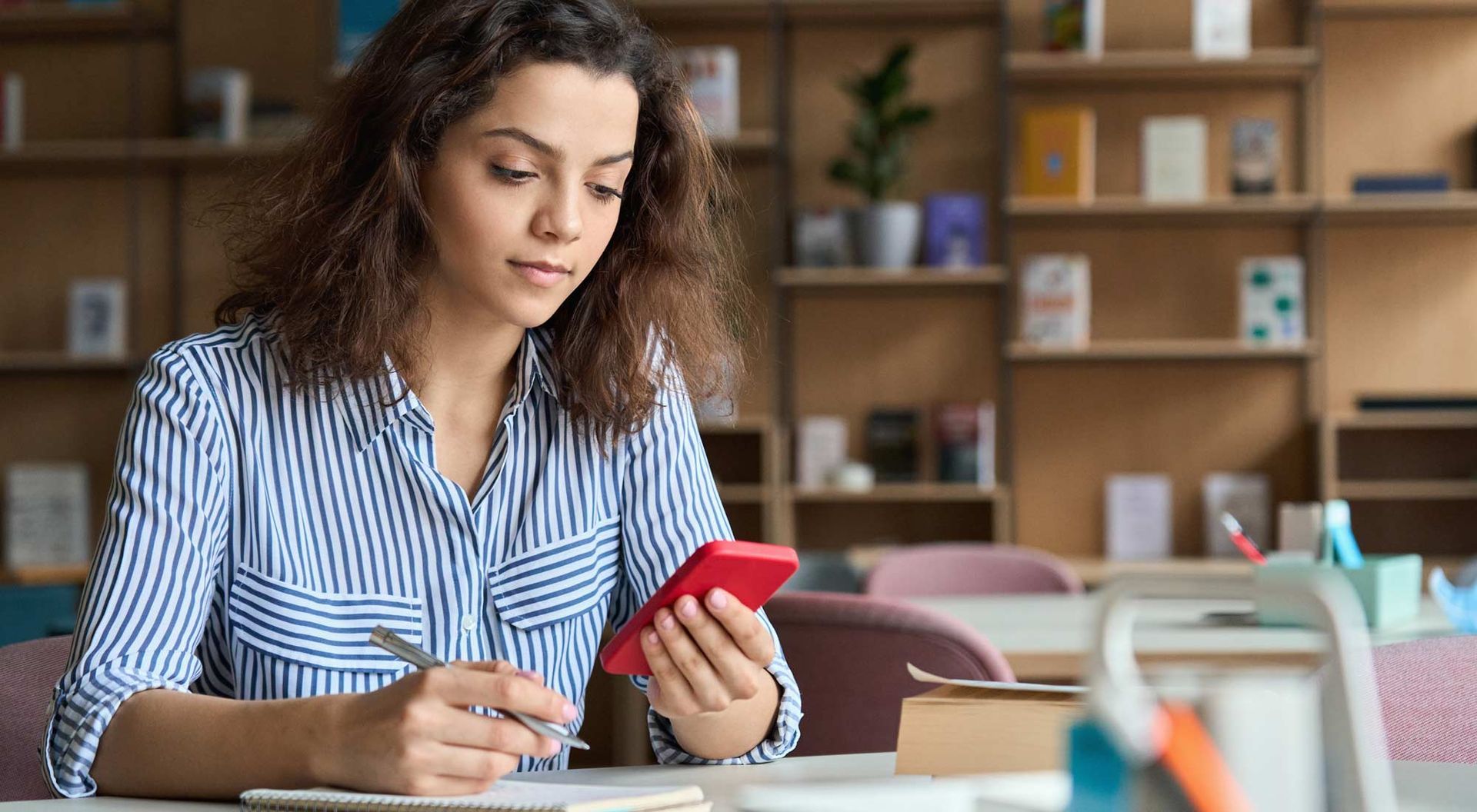 A woman is sitting at a desk looking at her cell phone. Utilizing Technology at College Fairs: Enhancing the Experience for Attendees