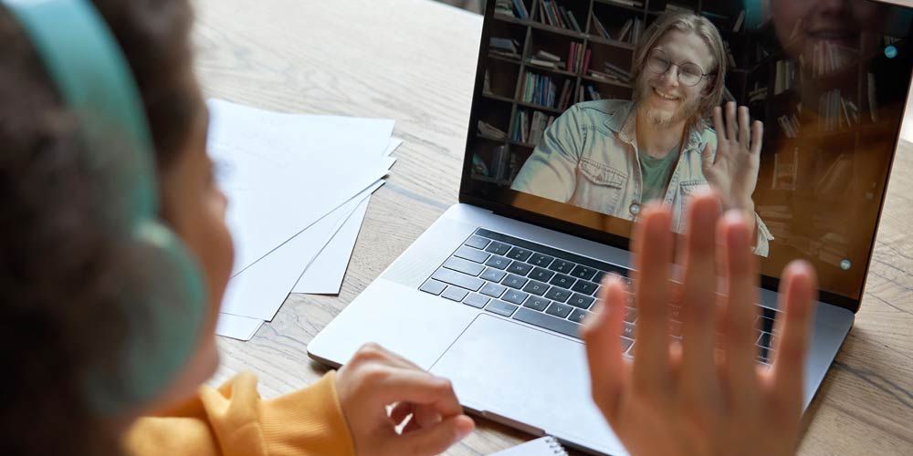 A student wearing headphones is having a video call on a laptop computer with her recruiter at her virtual college Fairs