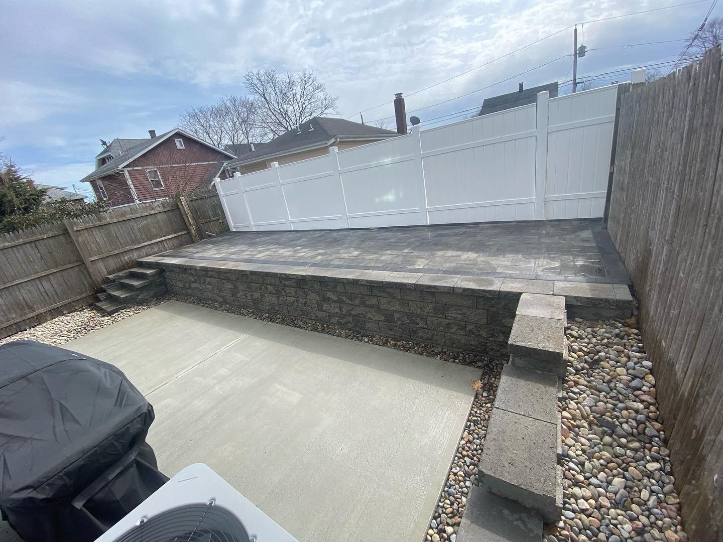 A backyard with a concrete patio , stairs , and a white fence.