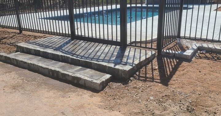 A concrete staircase leading to a pool behind a metal fence.