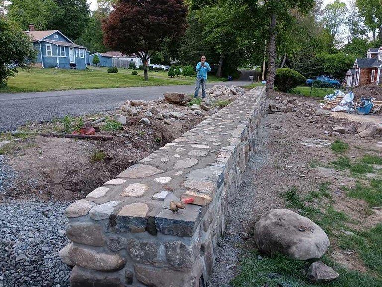 A man is standing next to a stone wall in a yard.