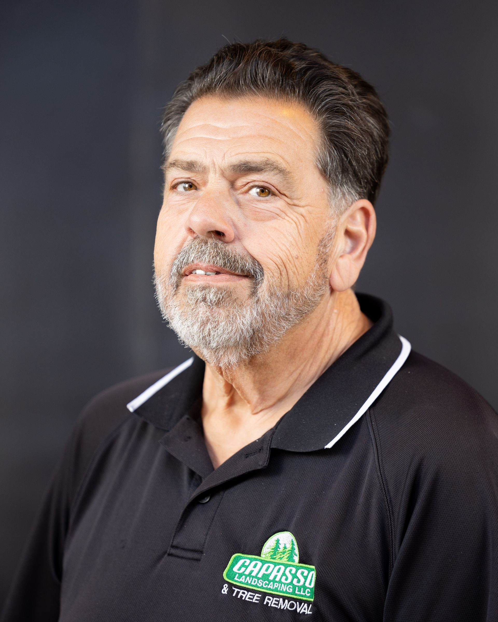 Portrait of a man in a black polo shirt against a dark background, wearing a slight smile