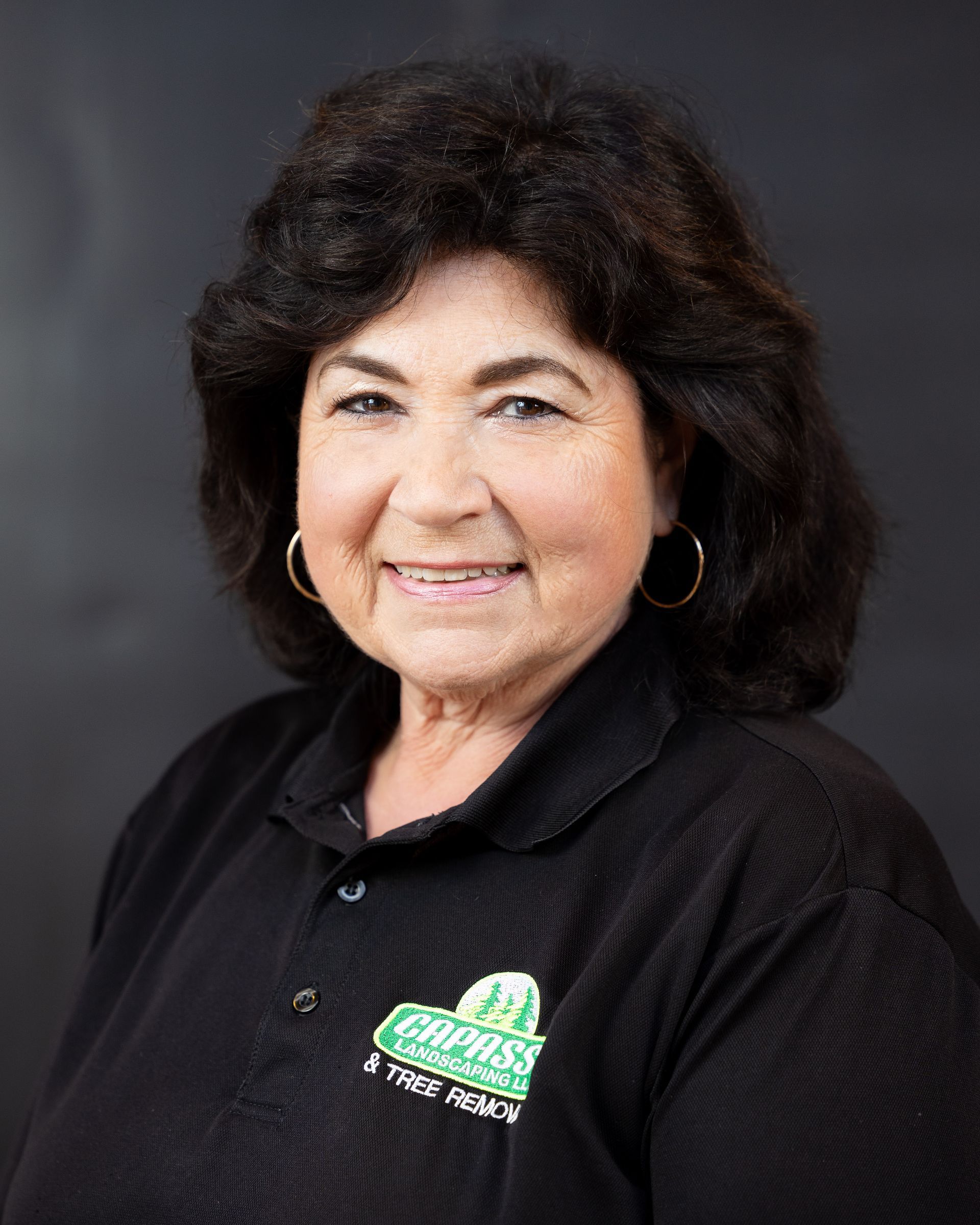 Portrait of a smiling woman in a black shirt with a logo, against a gray studio background