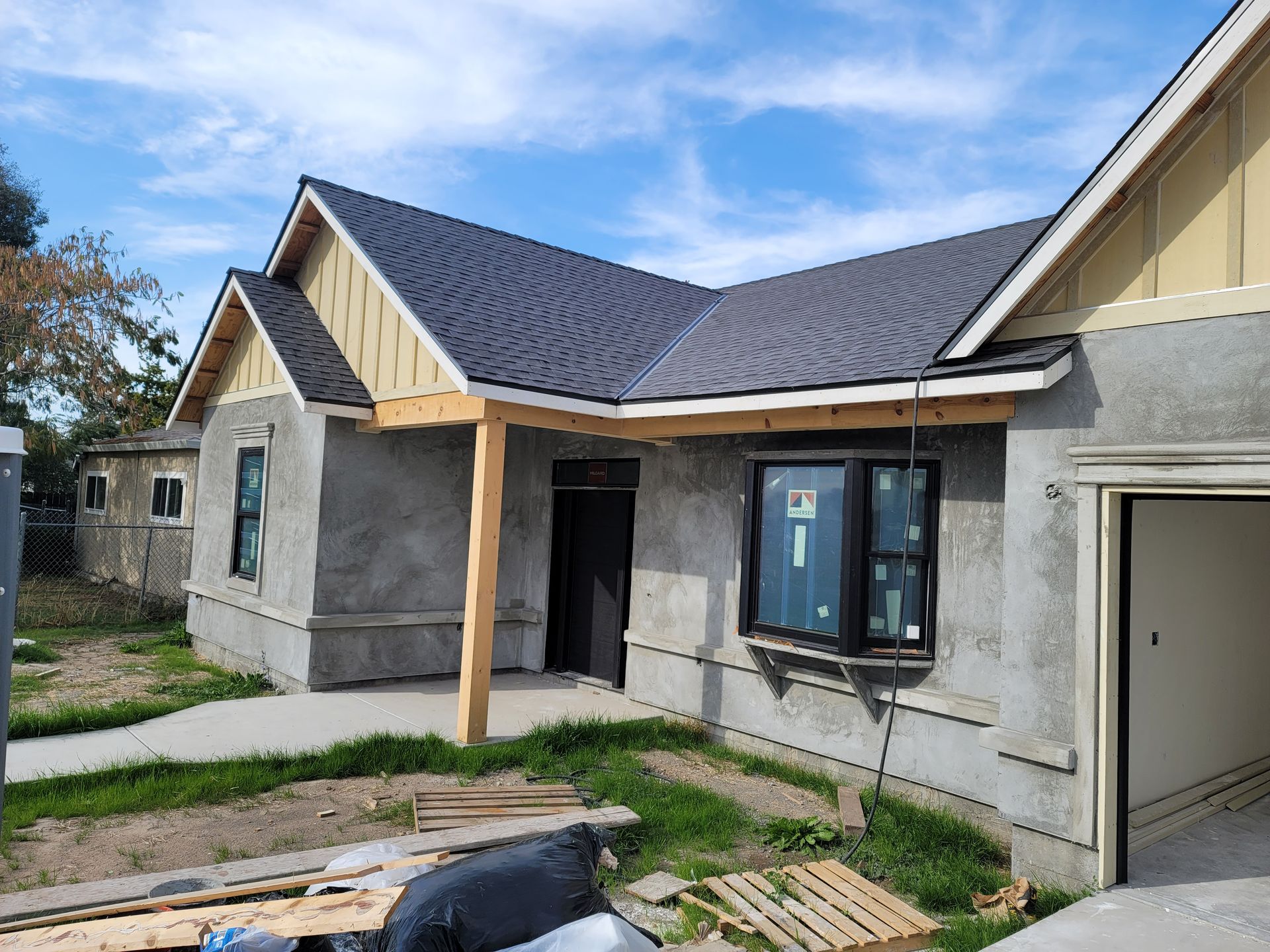 Partially finished house exterior with gray stucco walls, dark roof, and a covered entry porch