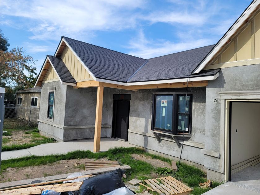 Partially finished house with gray stucco walls, dark roof, and a front porch under construction