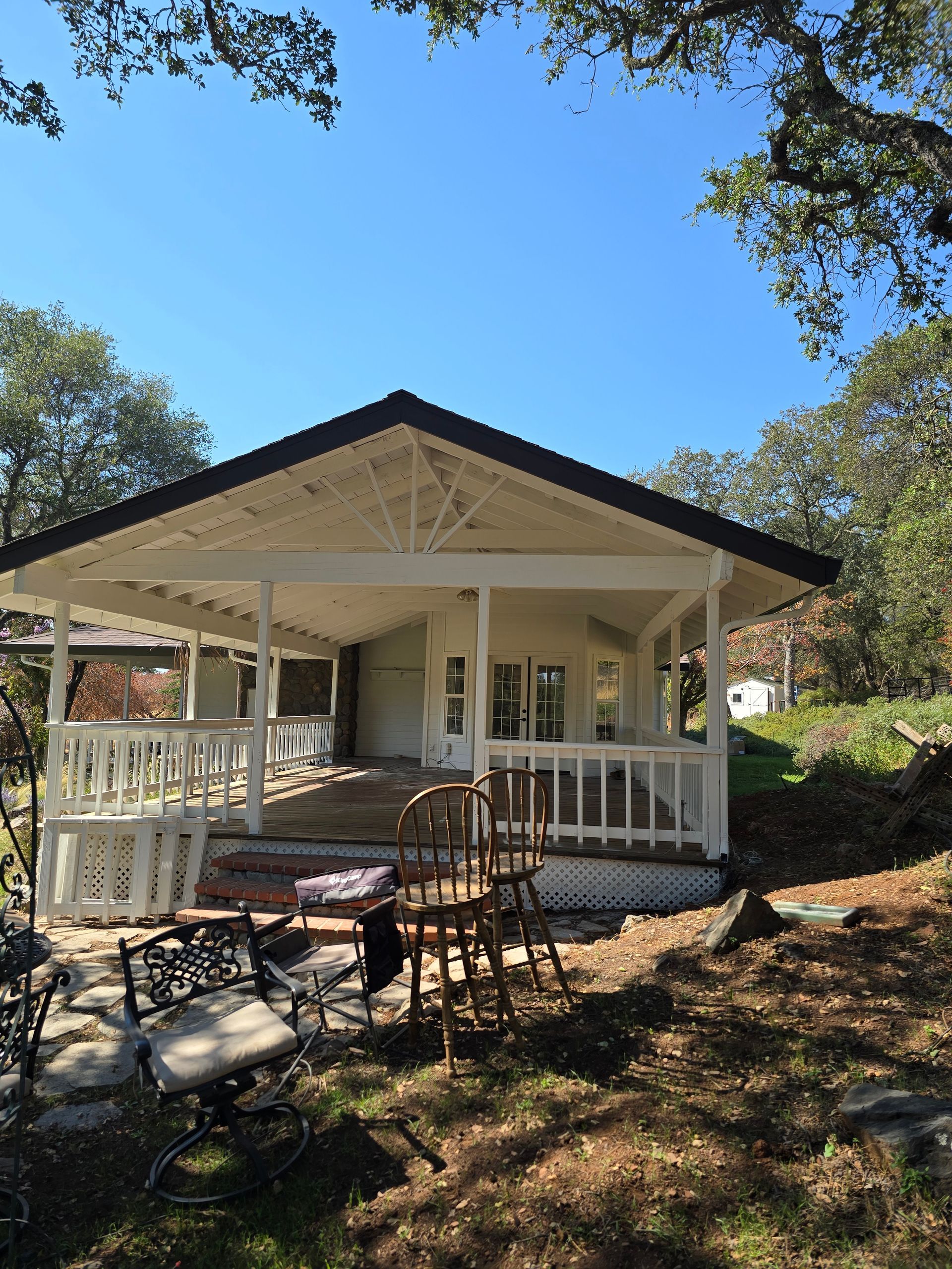 White cottage porch with rocking chairs and stone patio under trees on a sunny day