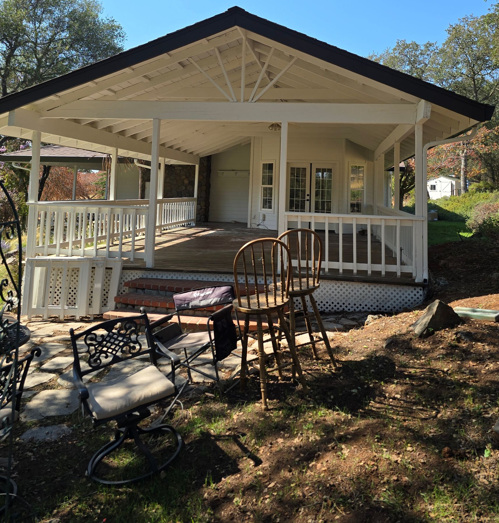 Porch with white railing and chairs, front of a house, with outdoor furniture in the yard
