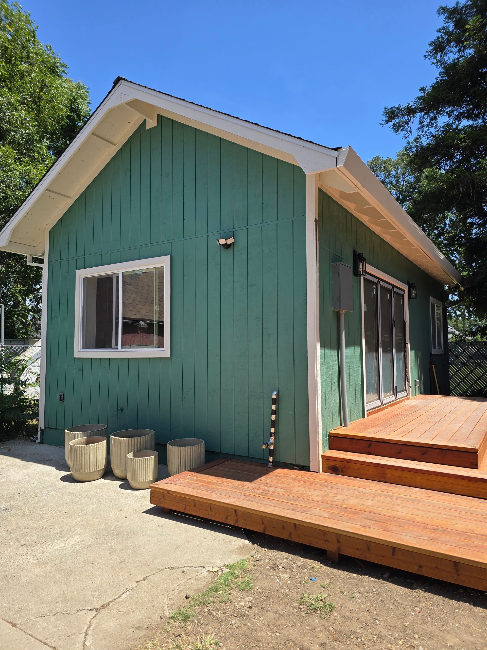 Green house exterior with white trim, wooden steps, and a concrete patio under a blue sky
