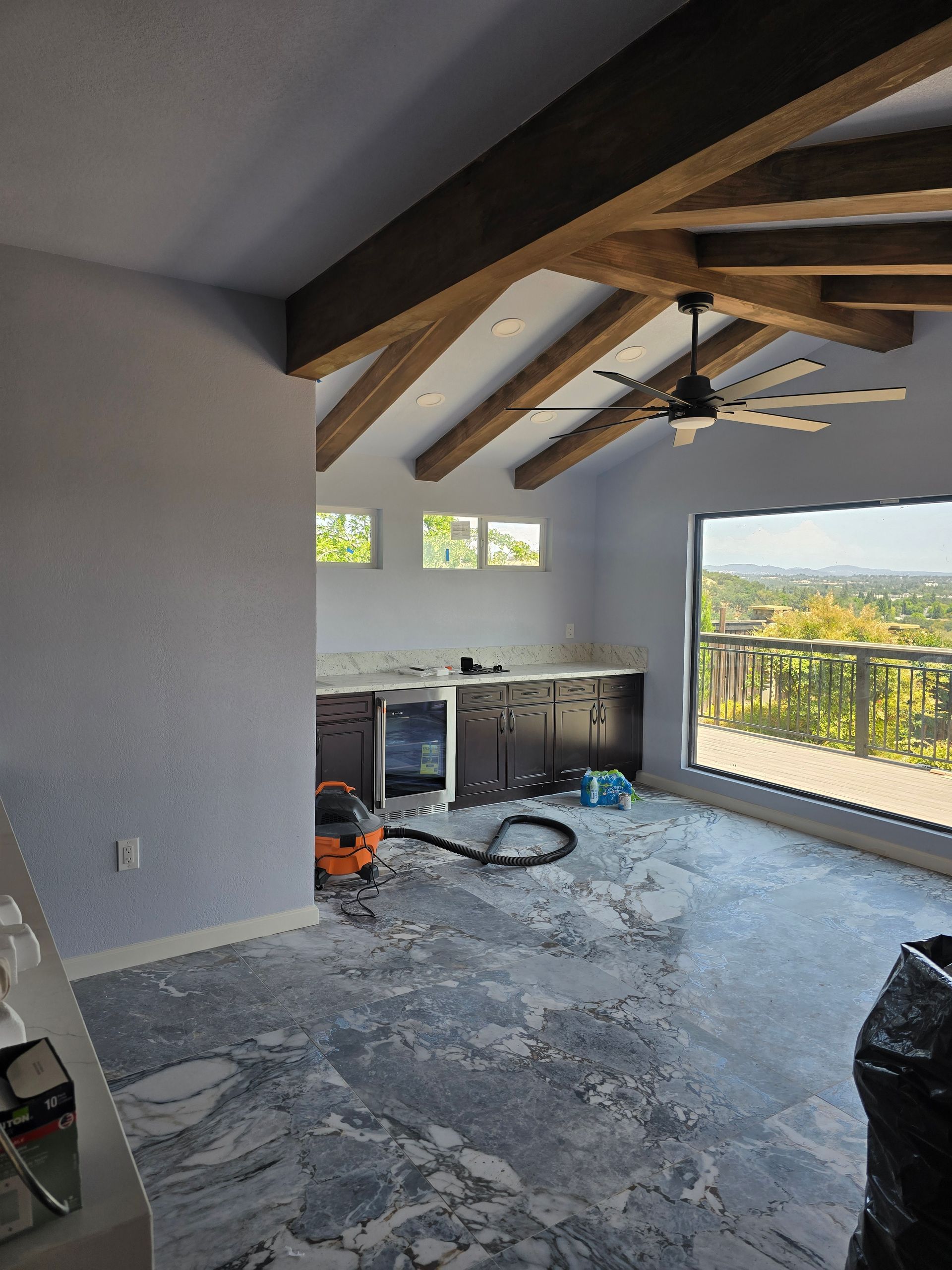 Renovation in progress: empty room with exposed beams, workbench, tools, and large balcony window.