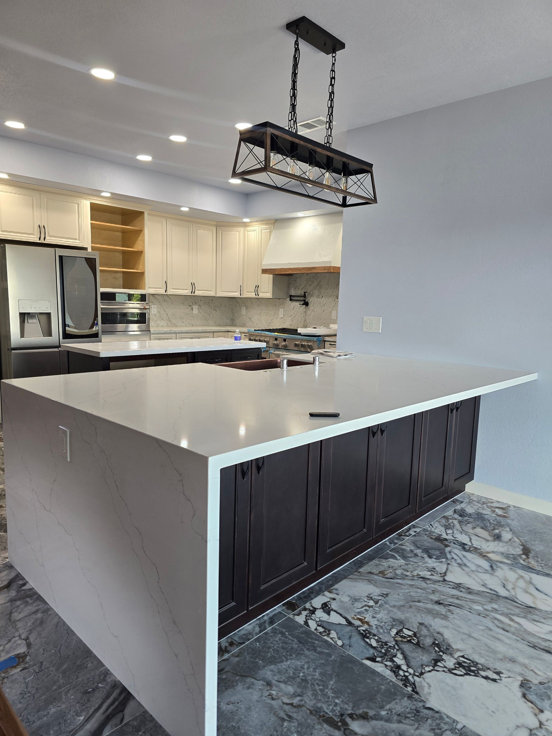 Modern kitchen with white cabinets, large island, pendant light, and gray marble floor