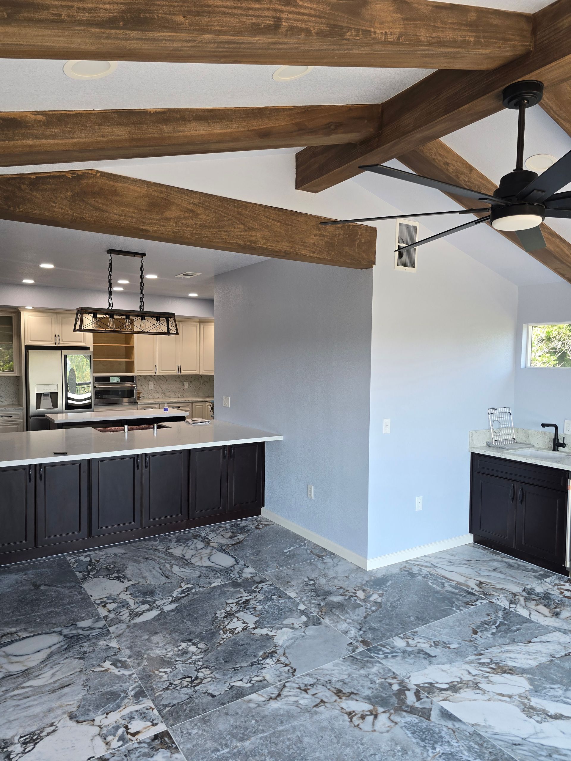 Modern kitchen with exposed wood beams, dark cabinets, gray tile floor, and ceiling fan