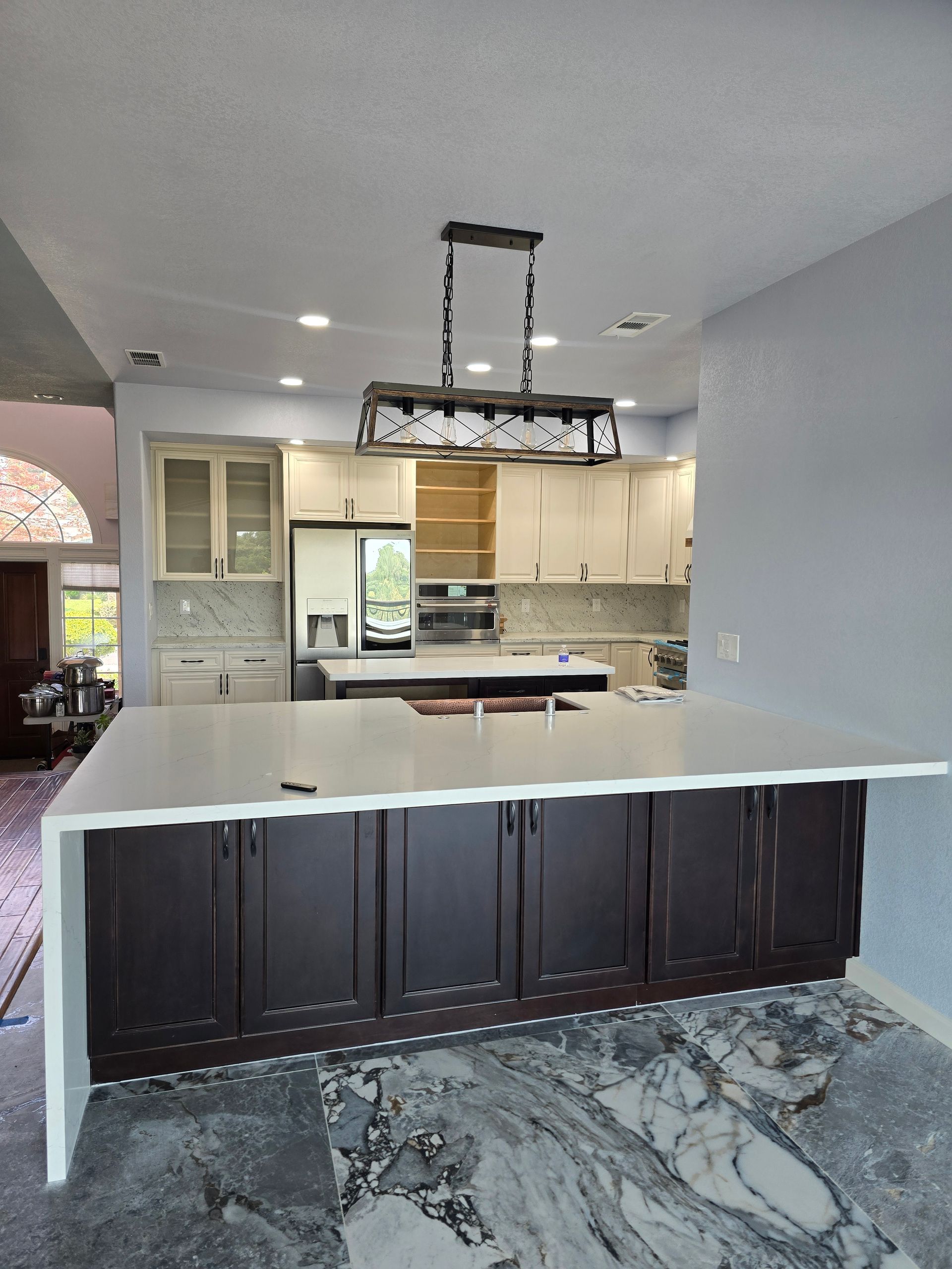 Modern kitchen with dark island cabinets, white countertops, and patterned tile floor; ceiling light fixture above.