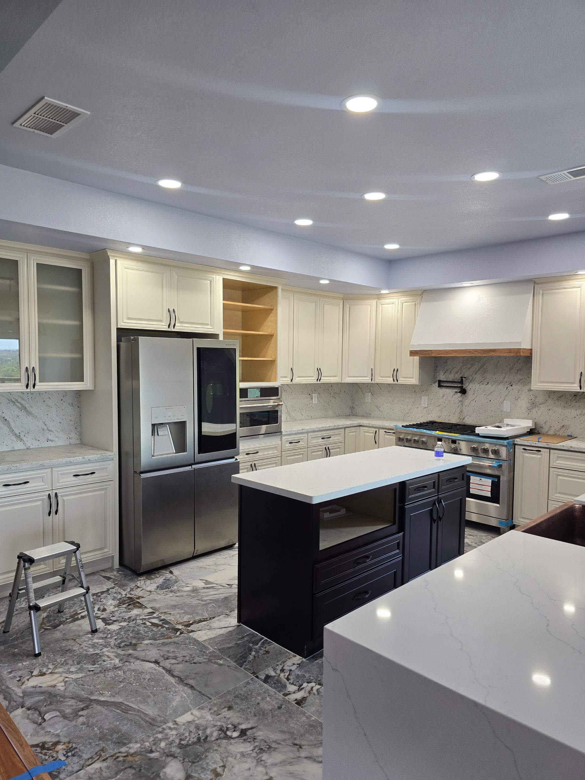 Modern kitchen with stainless steel fridge, white cabinets, and a large island under recessed lighting