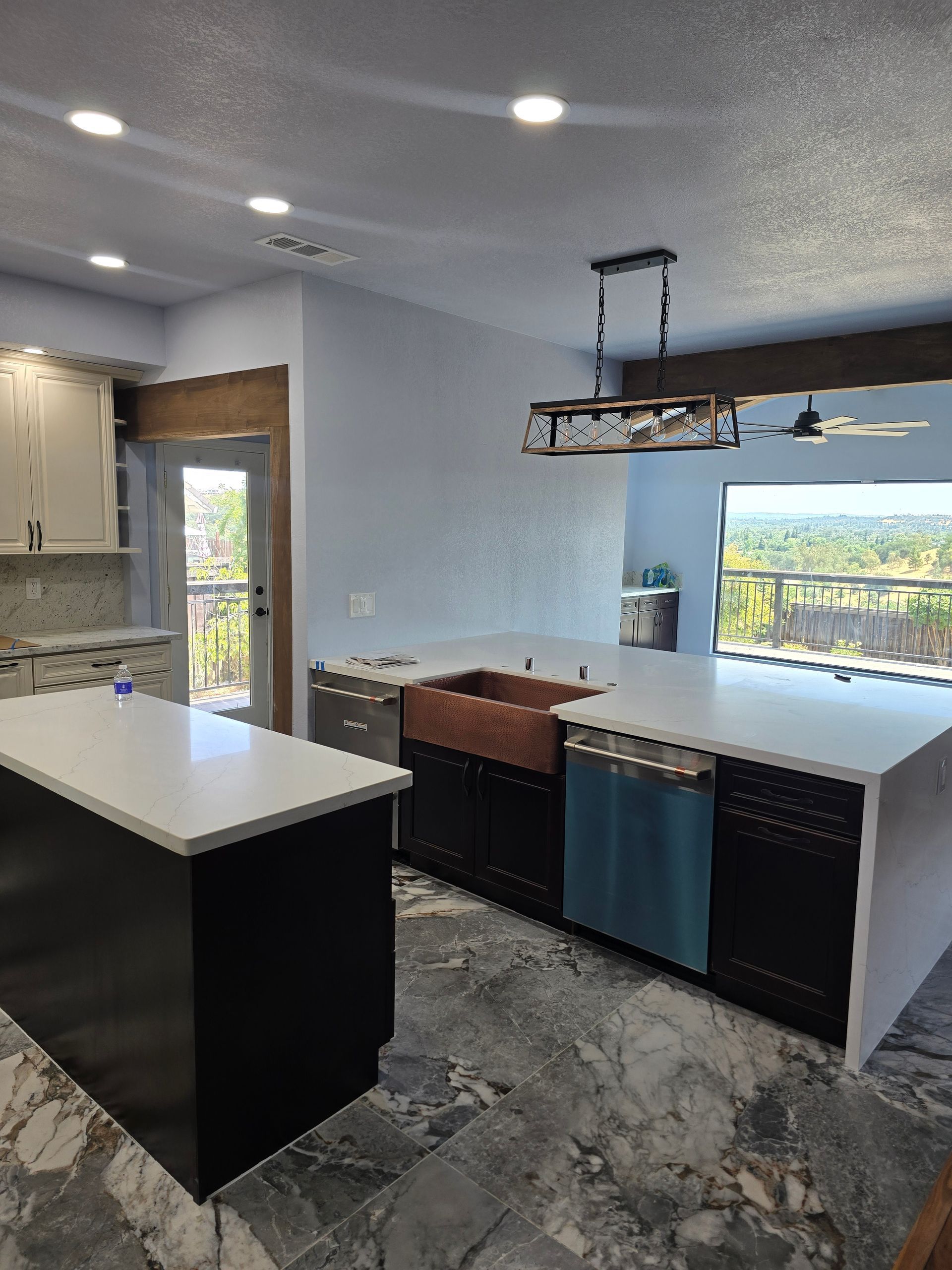 Modern kitchen with island, gray marble floors, pendant light, and large window over the sink
