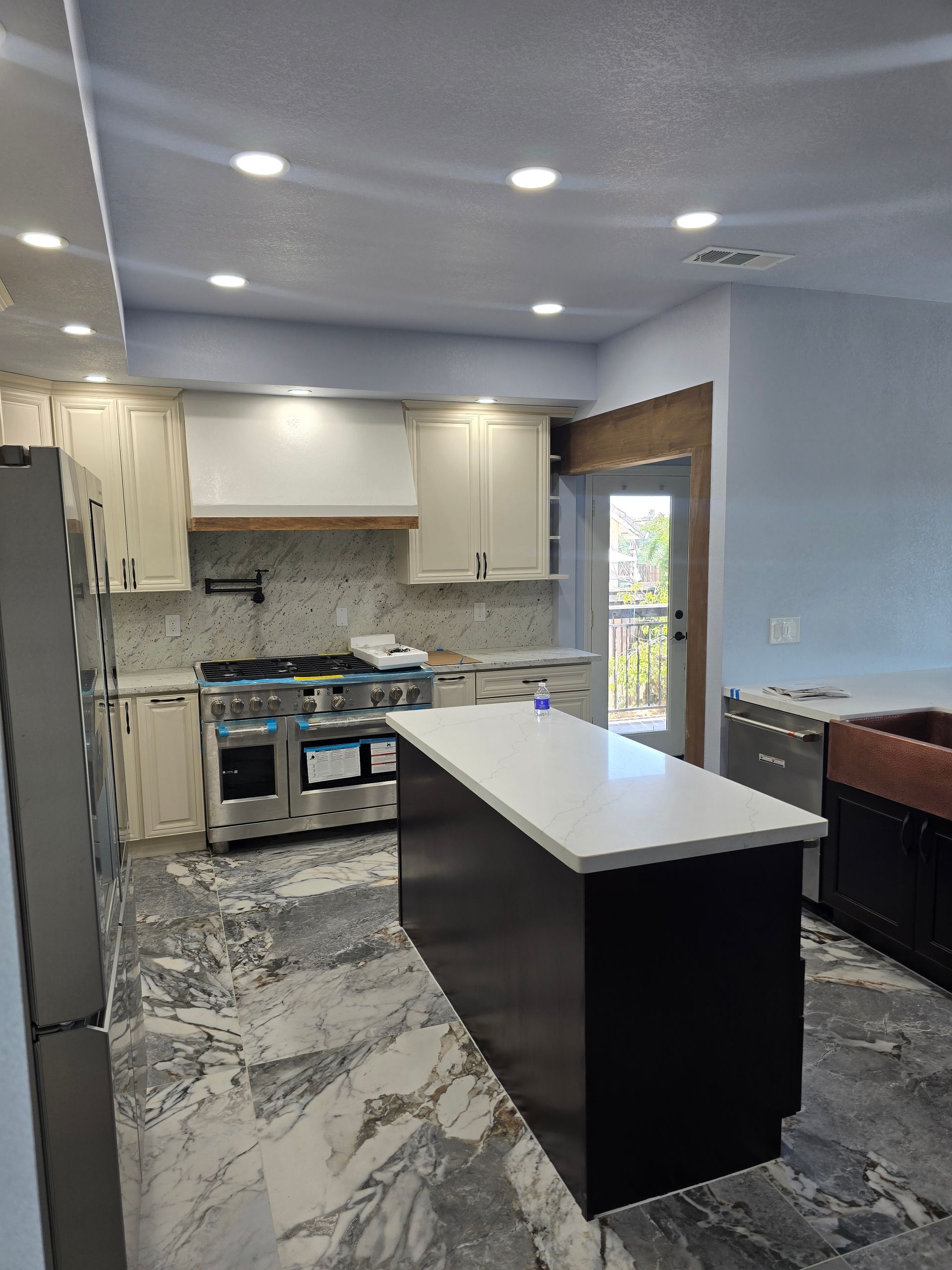 Modern kitchen with white cabinets, gray tile floor, island, stove, and recessed ceiling lights.