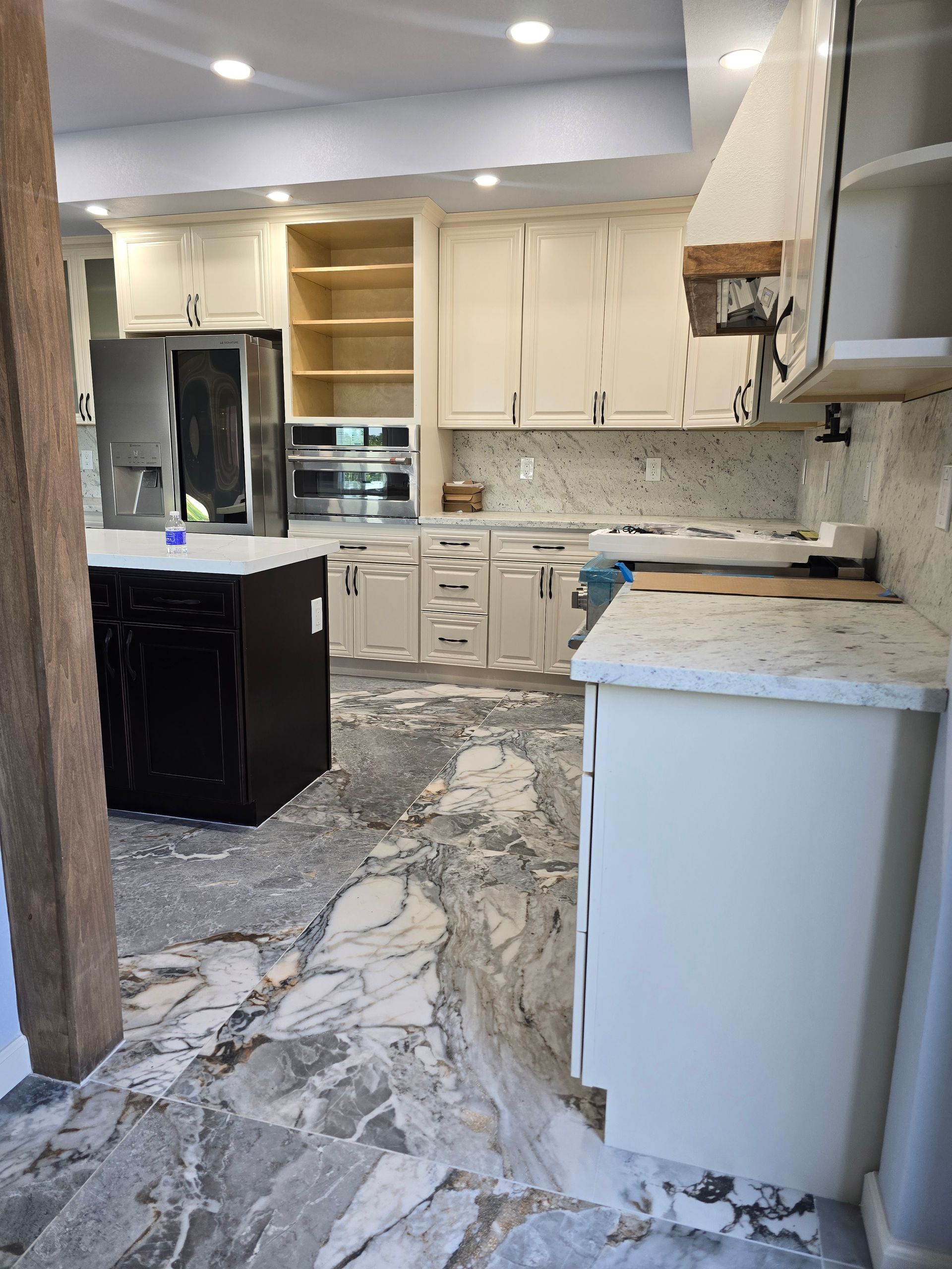 Modern kitchen with white cabinets, marble-look floor, black island, and built-in oven.