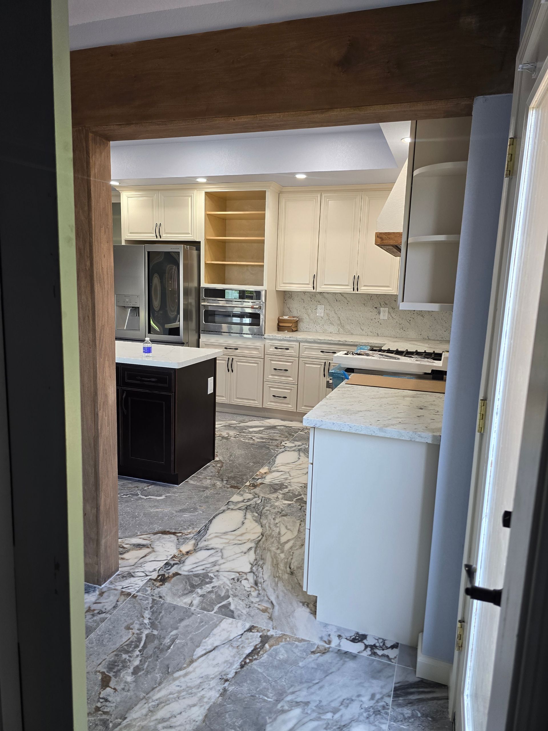 Partially renovated kitchen with broken tile floor, exposed cabinets, and a refrigerator under construction