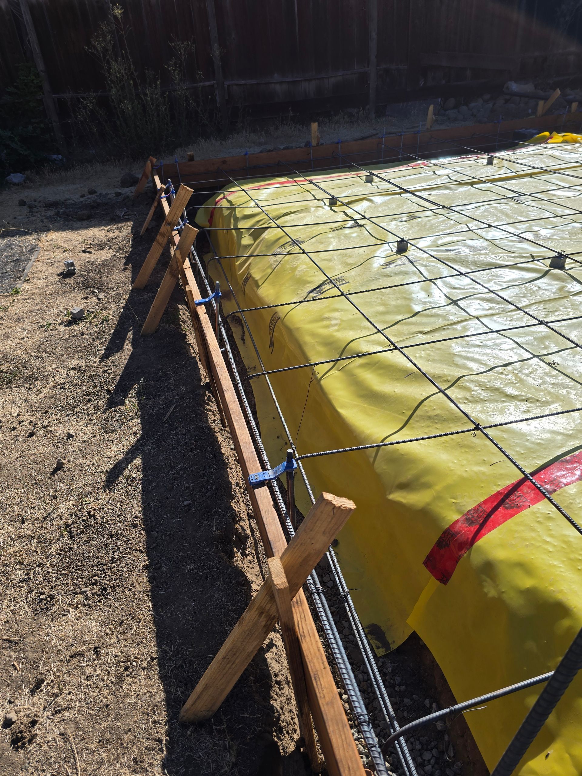 Yellow-covered foundation form with wire mesh and wooden stakes in a gravel yard