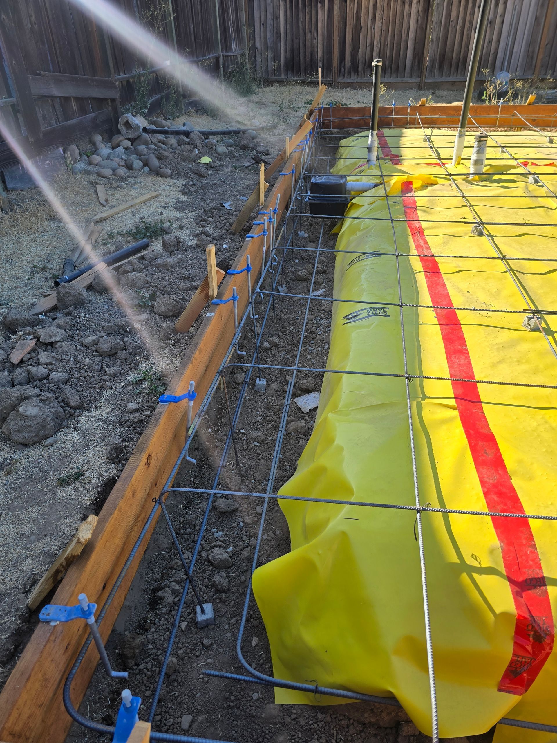 Construction site with yellow tarp-covered trench, rebar, and a red marking line in wet ground