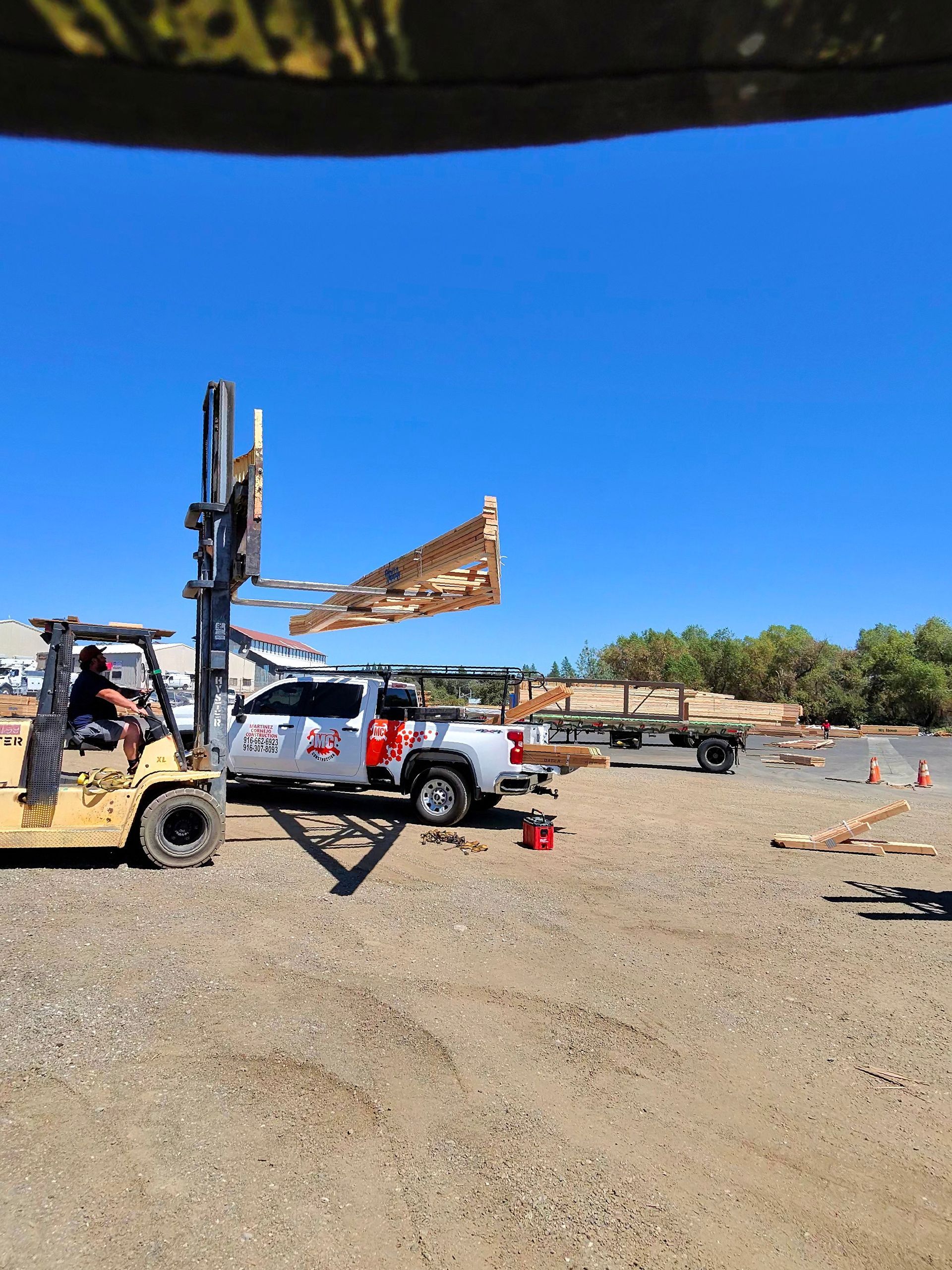 Forklift lifting a large sign beside a white pickup at a dusty outdoor lot under a clear blue sky