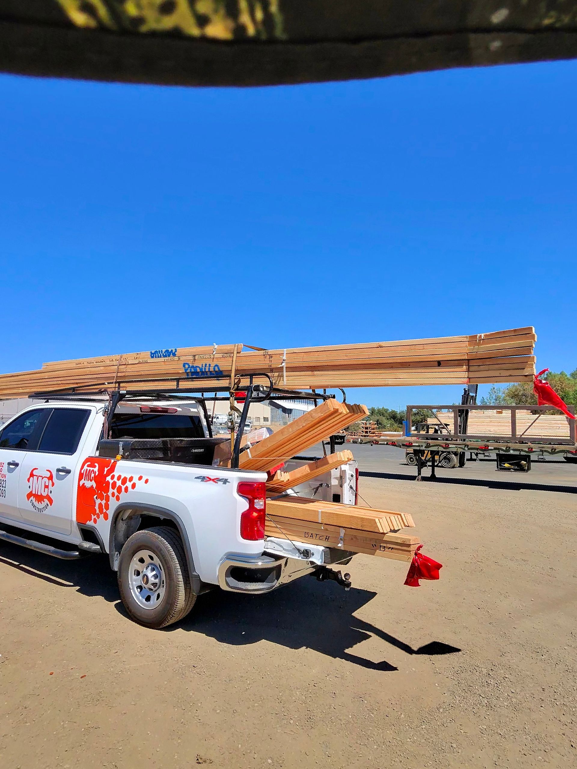 White pickup truck loaded with wooden planks on a sandy site under a blue sky