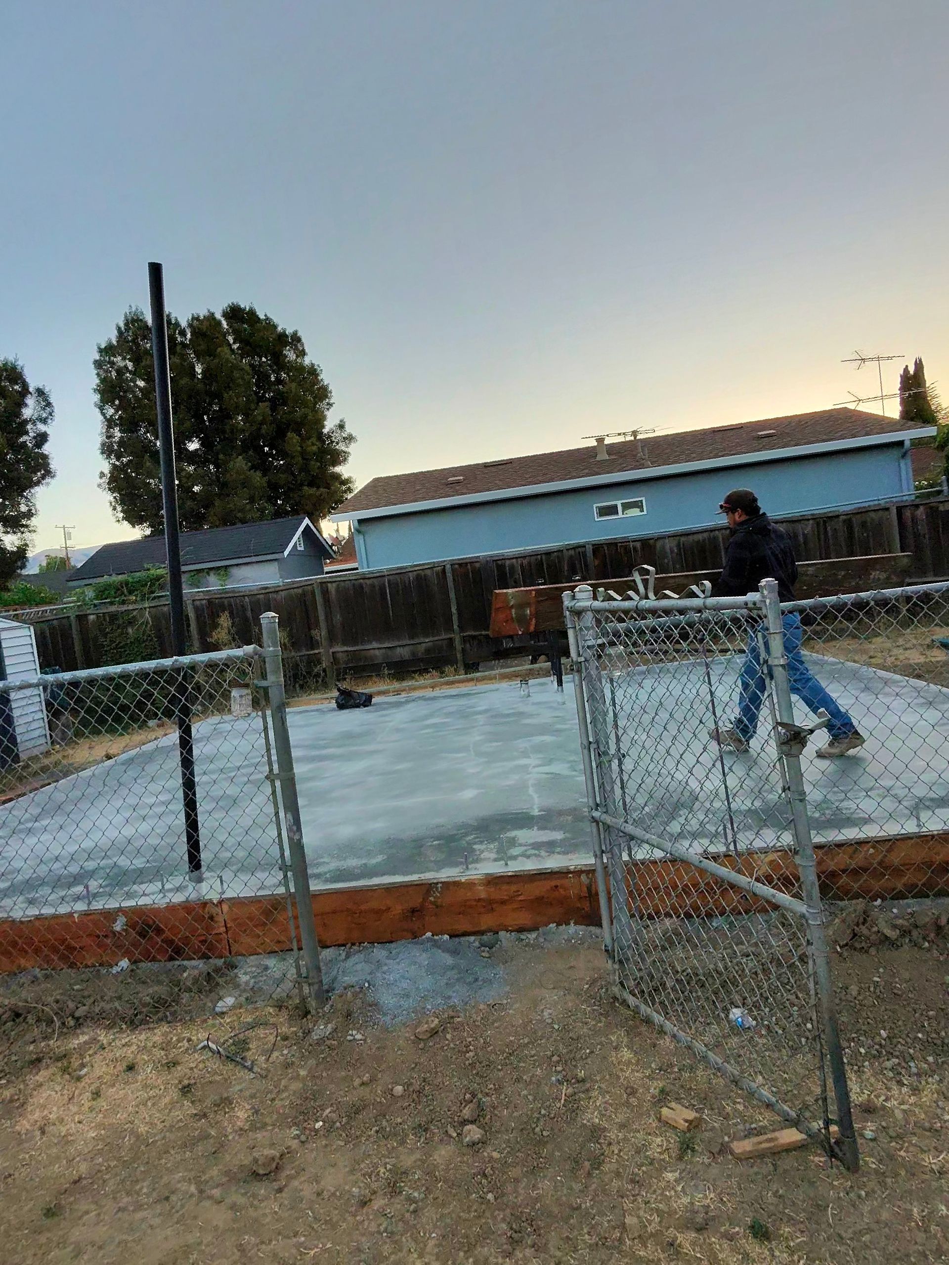 Chain-link fence around a construction site at dusk, with workers and a building in the background