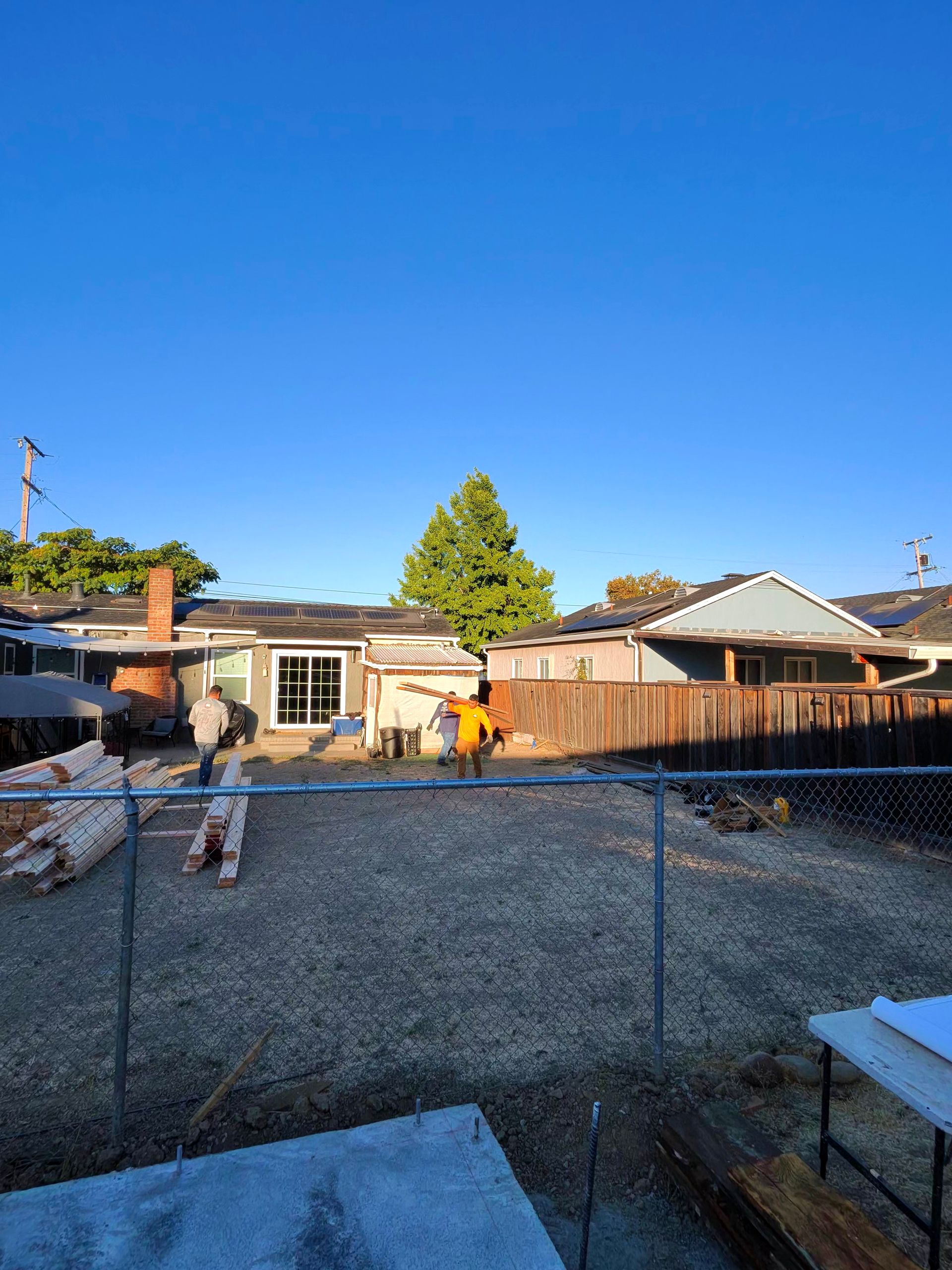 Backyard with chain-link fence, gravel ground, and a person near a small shed under a clear blue sky