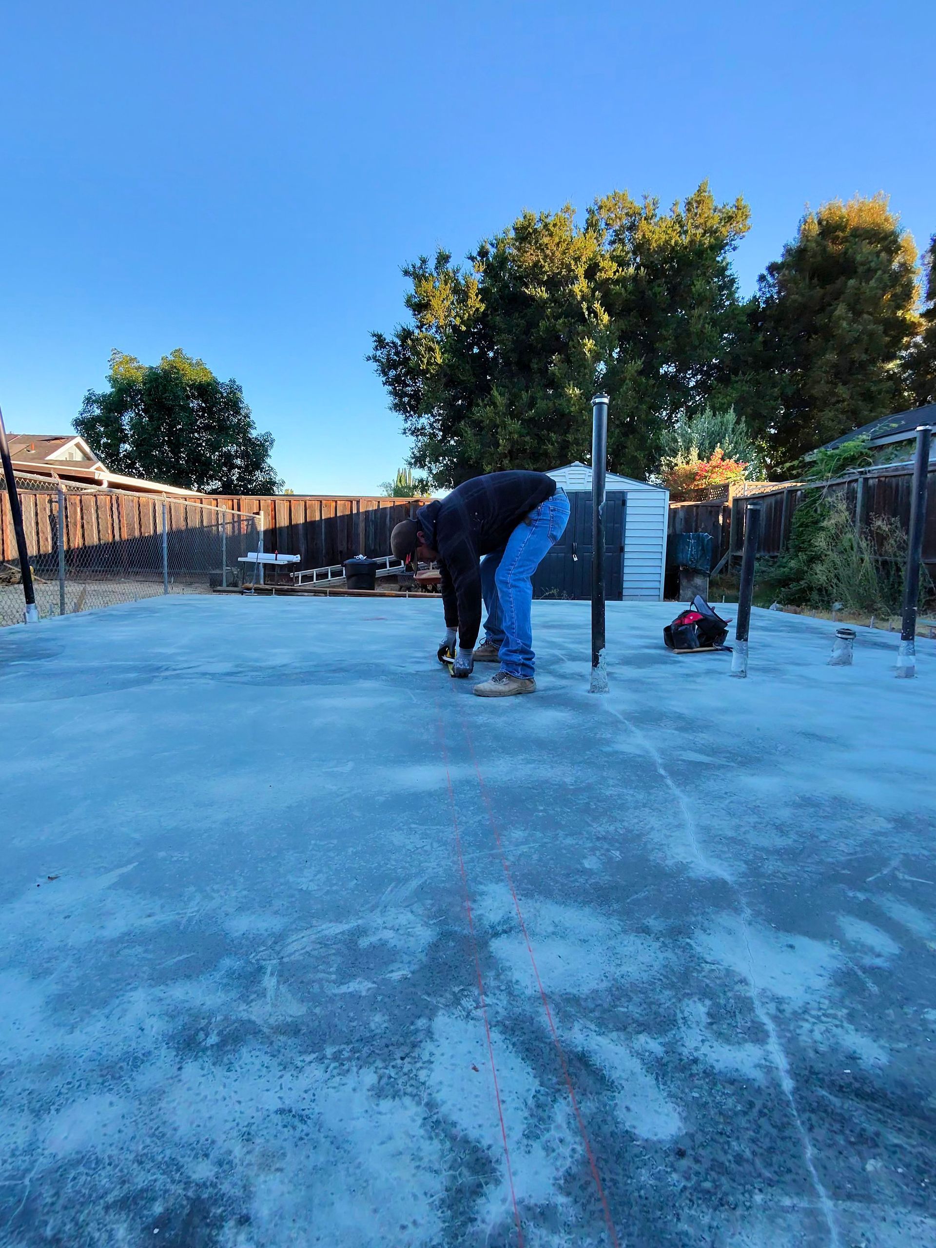 Person shoveling an icy driveway beside a snowblower under a clear blue sky
