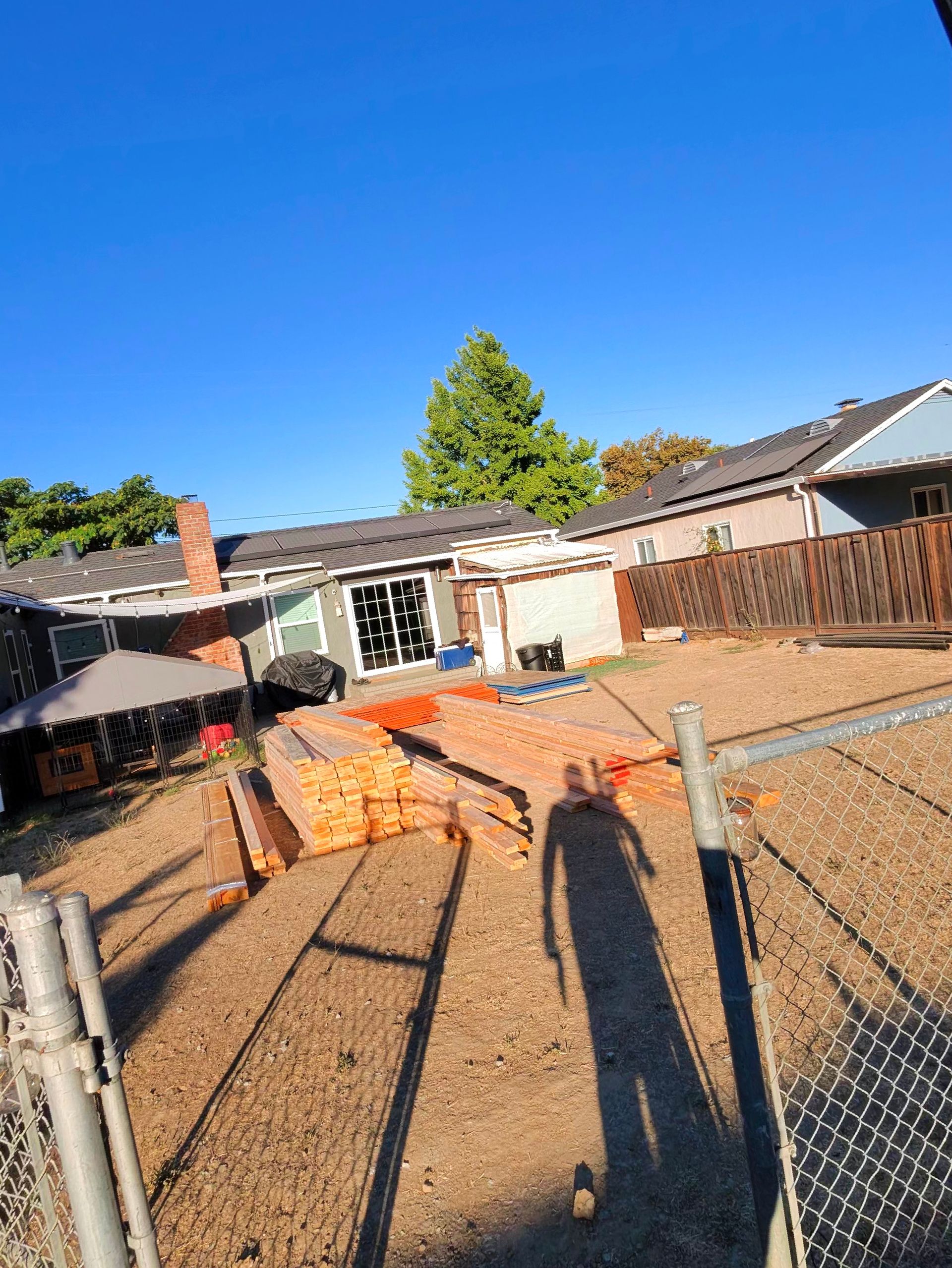 Backyard with gravel ground, orange fencing, a patio, and a house under a clear blue sky