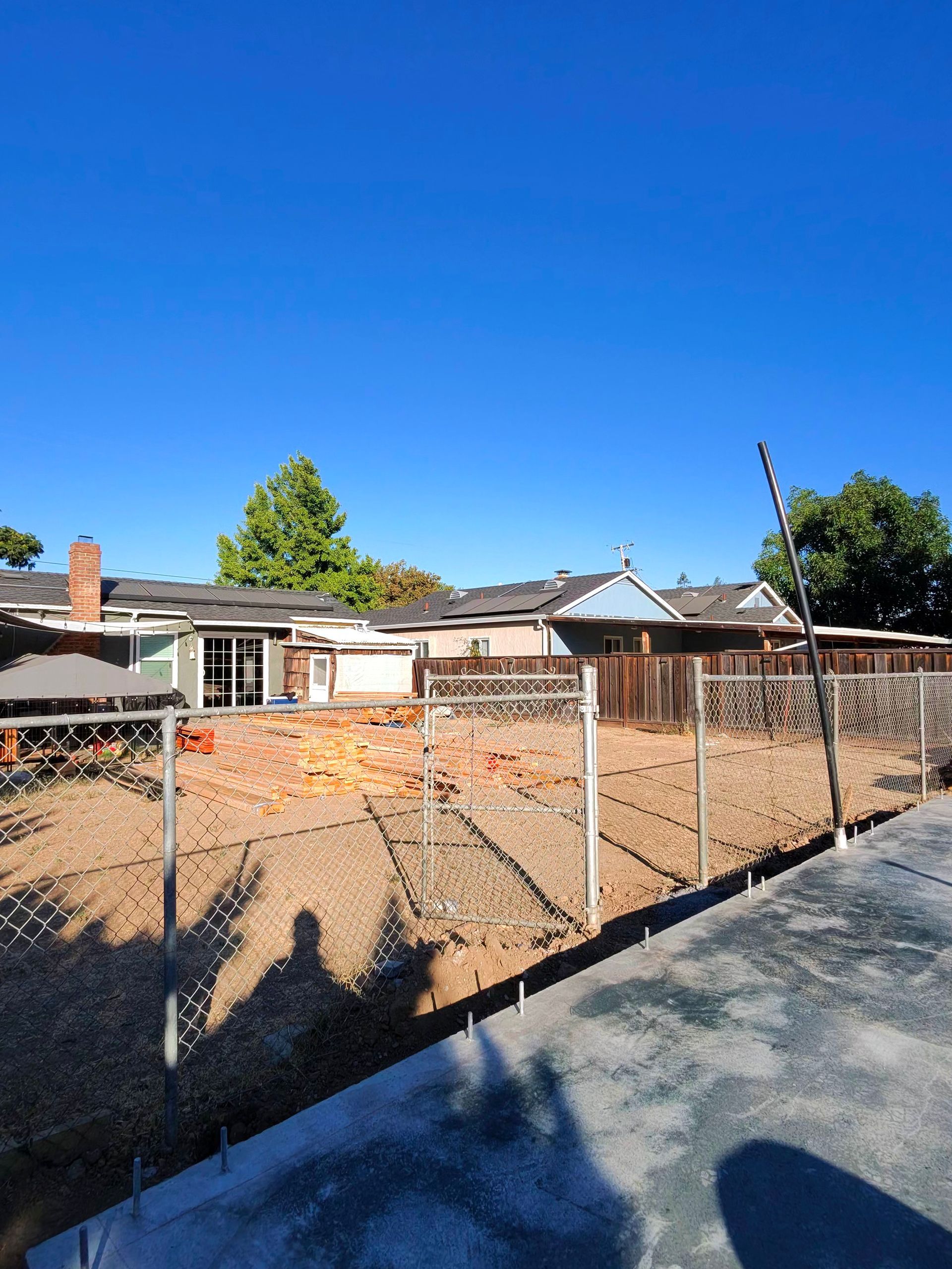 Partially demolished house lot behind chain-link fence under a clear blue sky