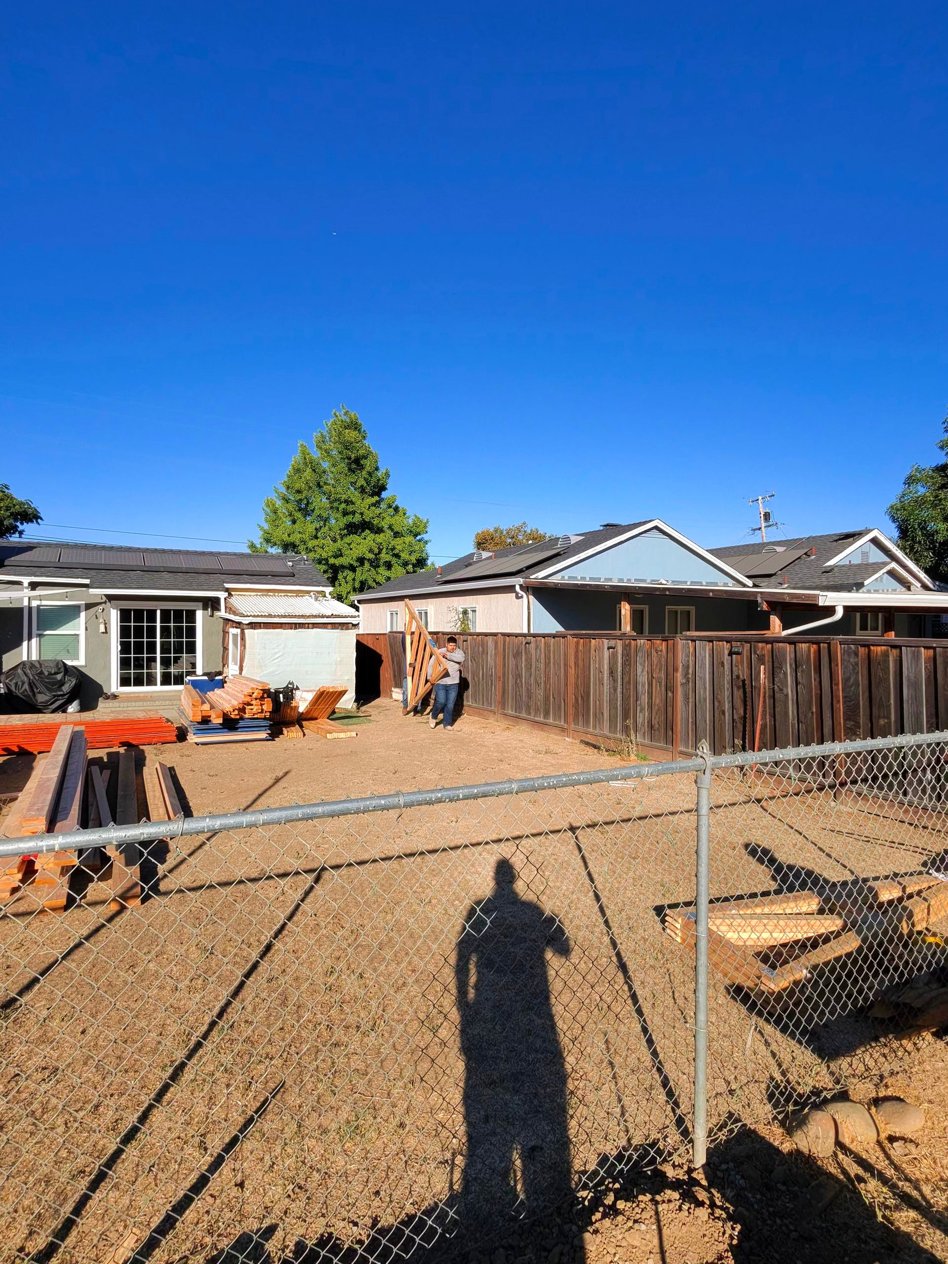 Backyard with gravel ground, chain-link fence, houses, and a clear blue sky