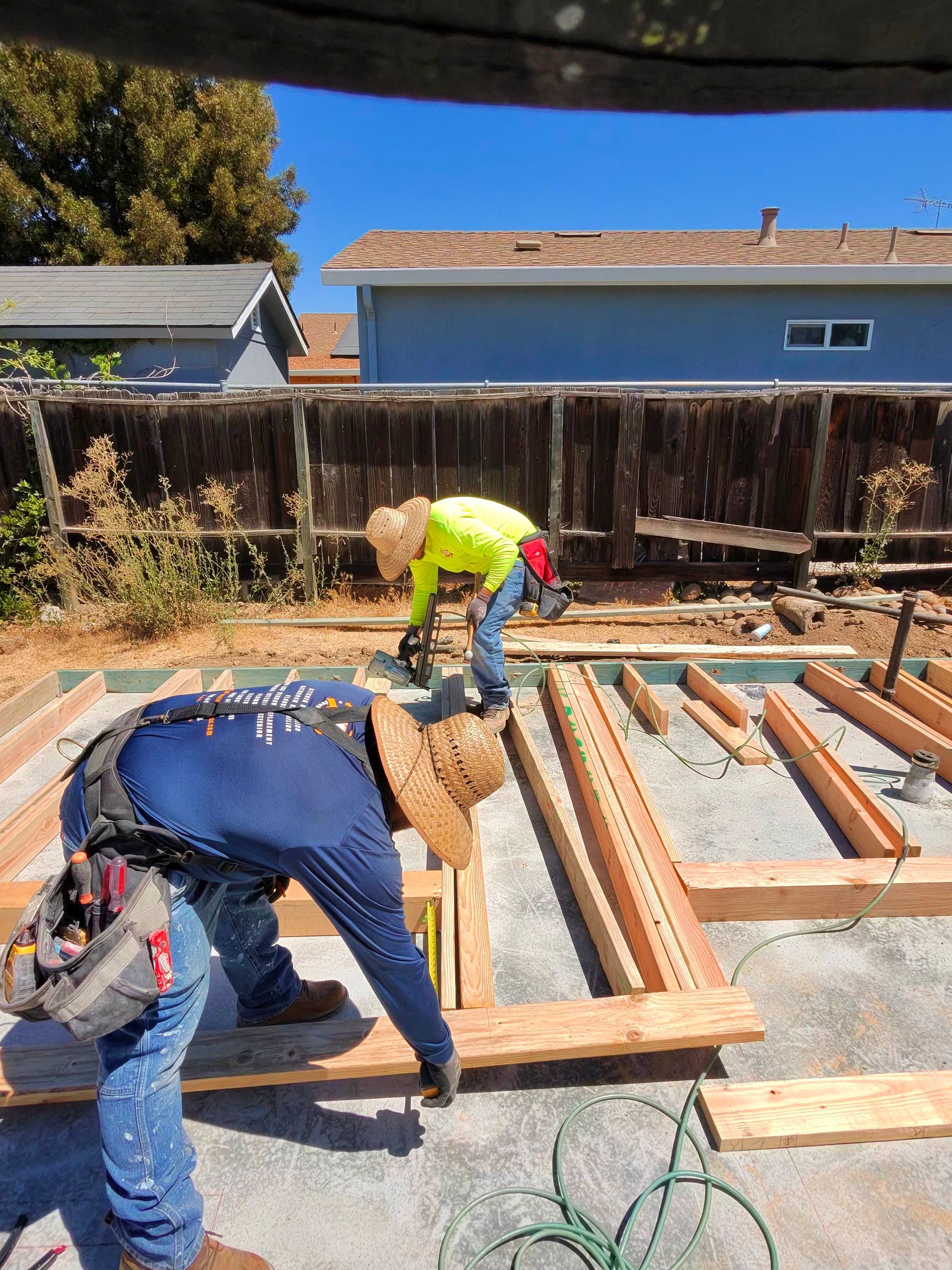 Two workers framing a wooden deck foundation in a backyard under construction.