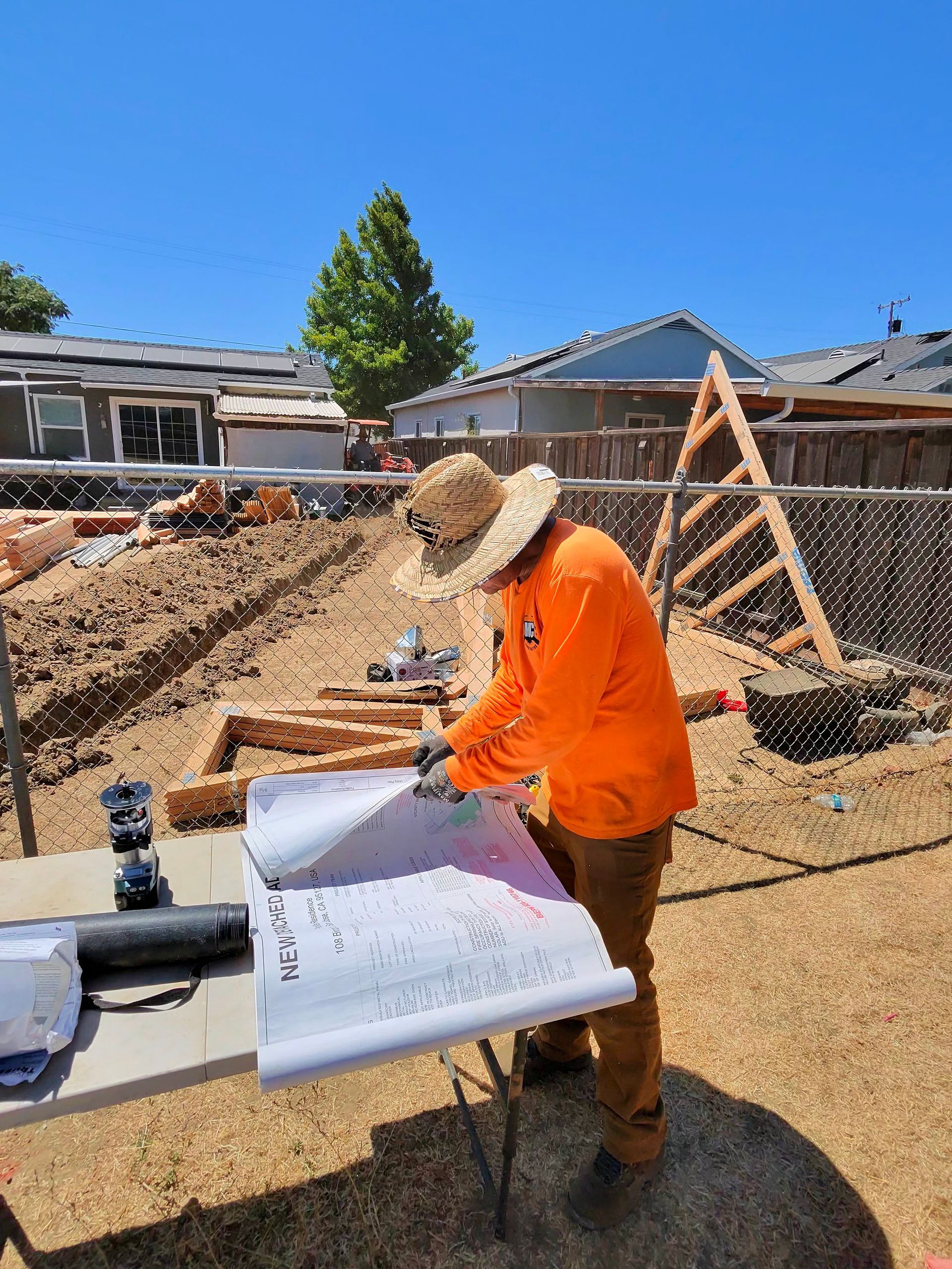 Worker in orange shirt reviewing plans at a construction site under a blue sky
