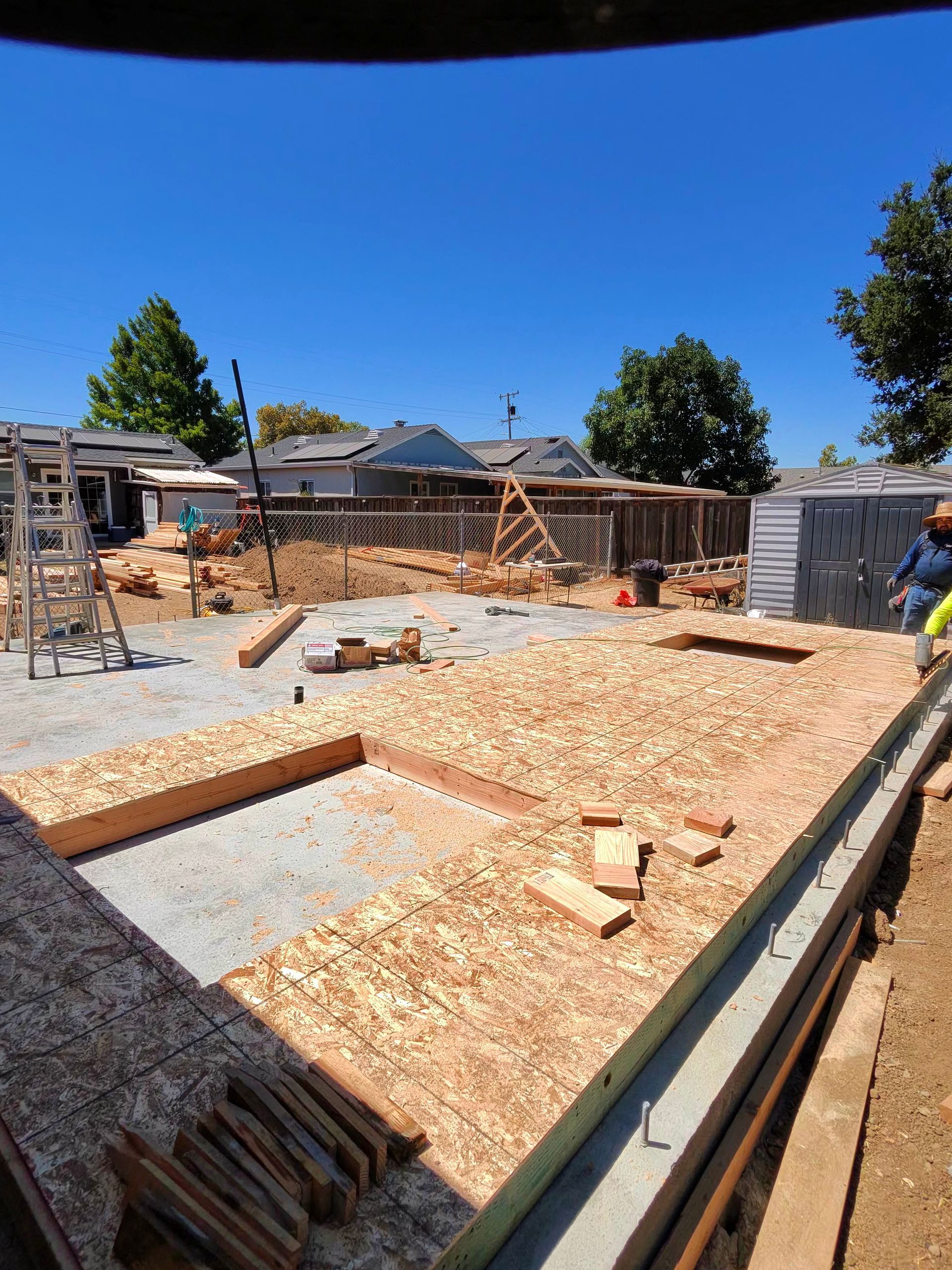 Construction site with foundation forms, lumber piles, and a worker under a bright blue sky