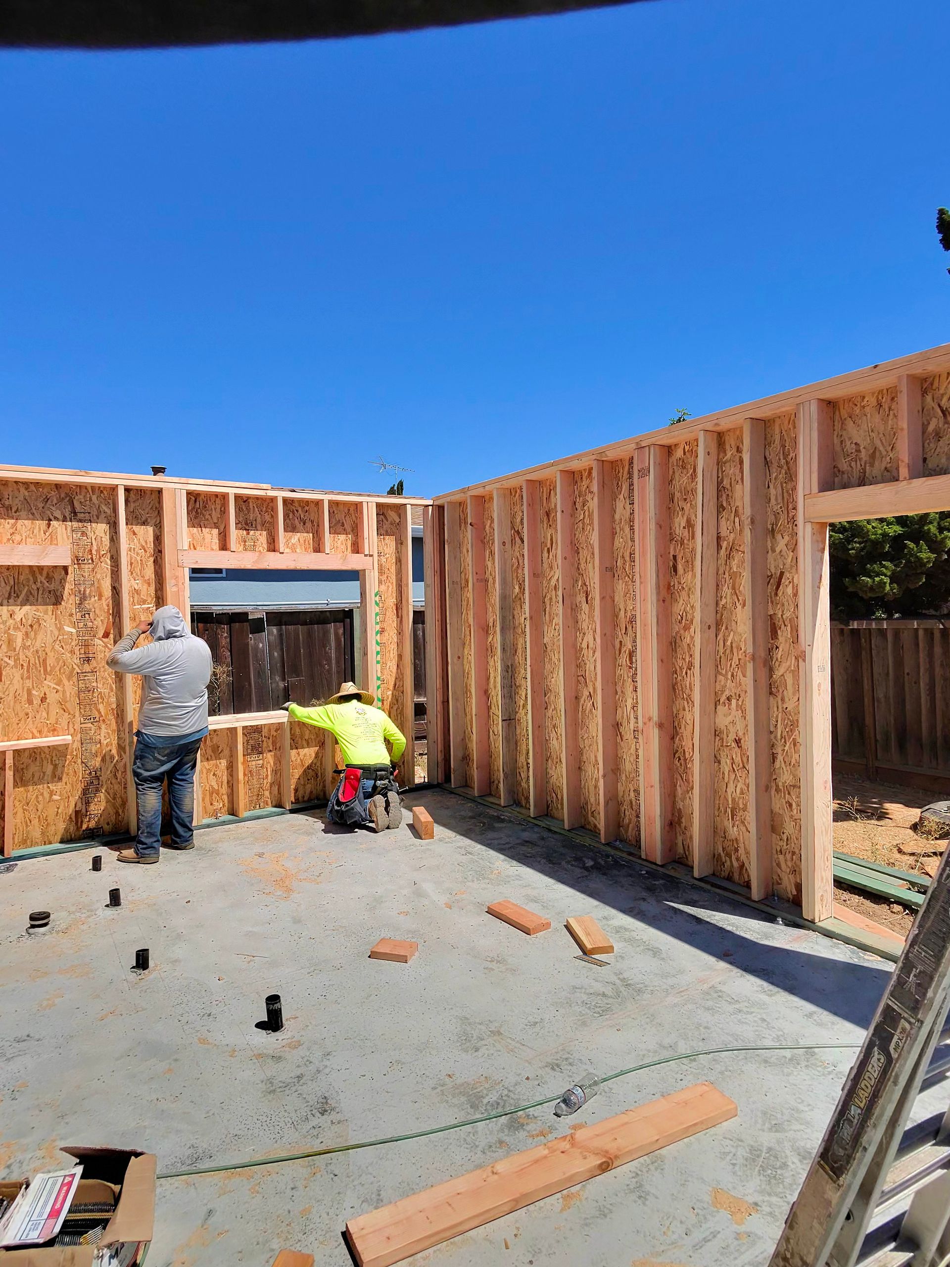 Workers framing the walls of a house under construction against a blue sky