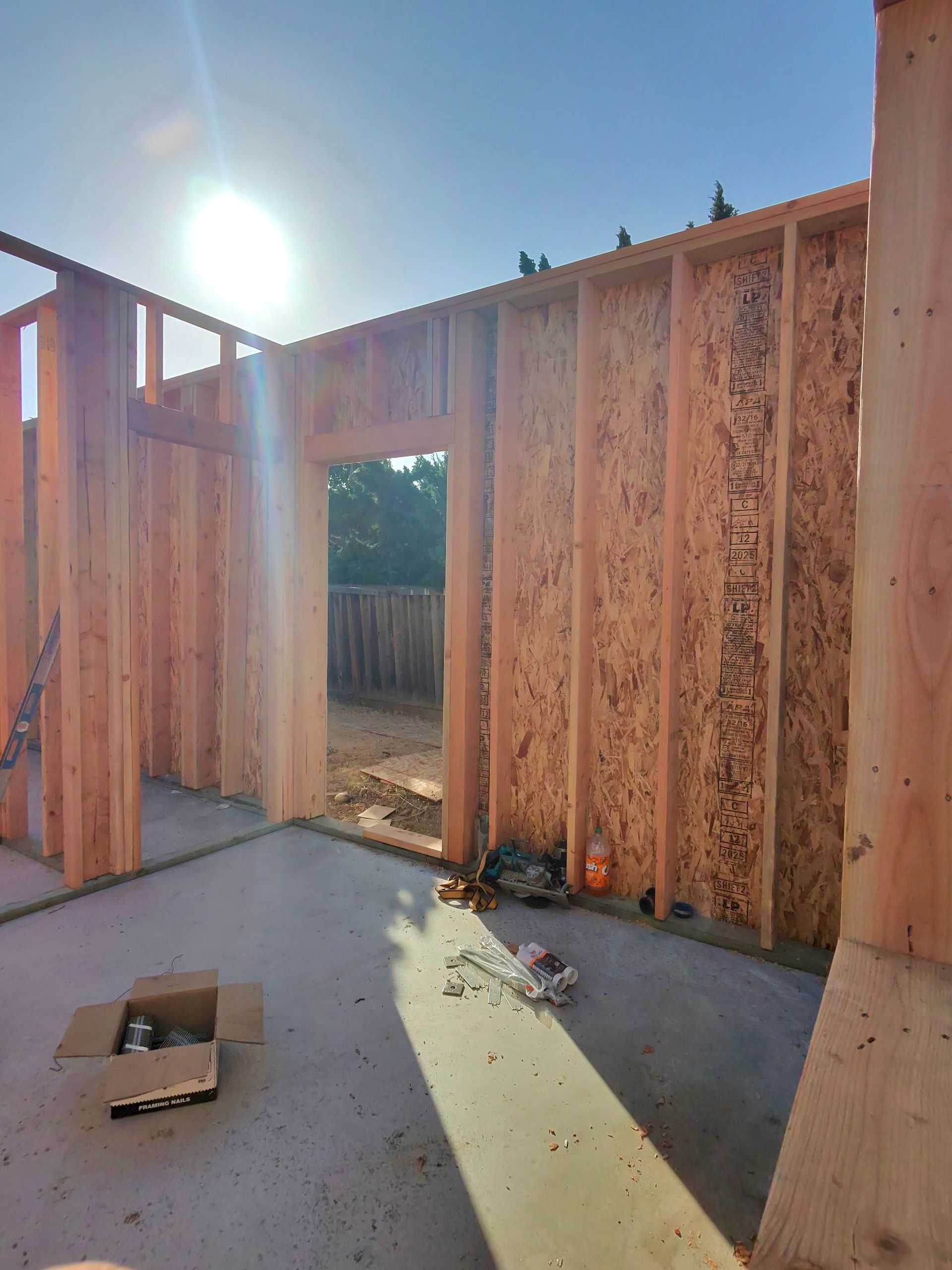 Sunlit wooden wall framing a doorway in an unfinished construction site with tools and debris on the floor