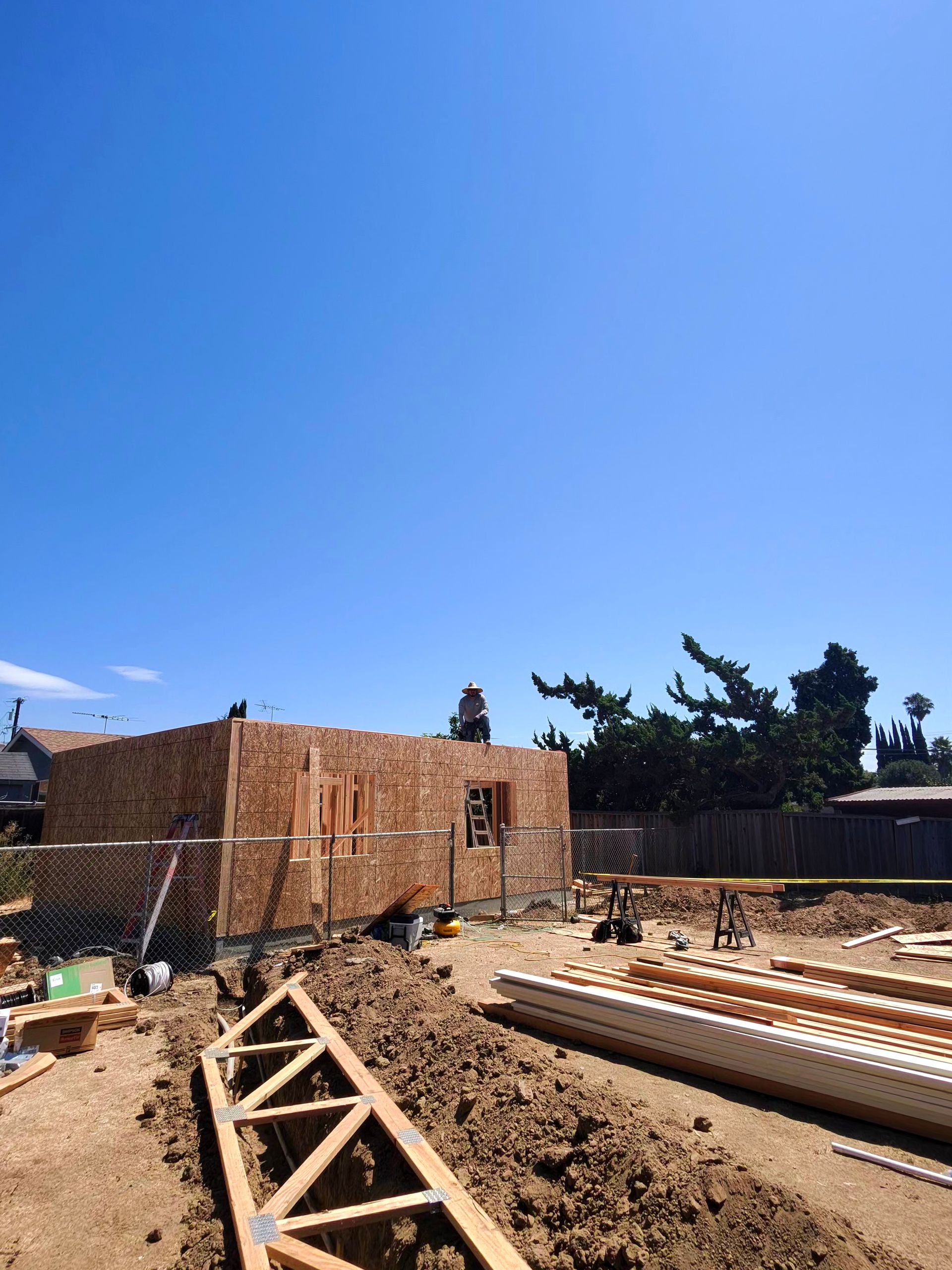Construction site with brick walls, dirt ground, stacked lumber, and clear blue sky