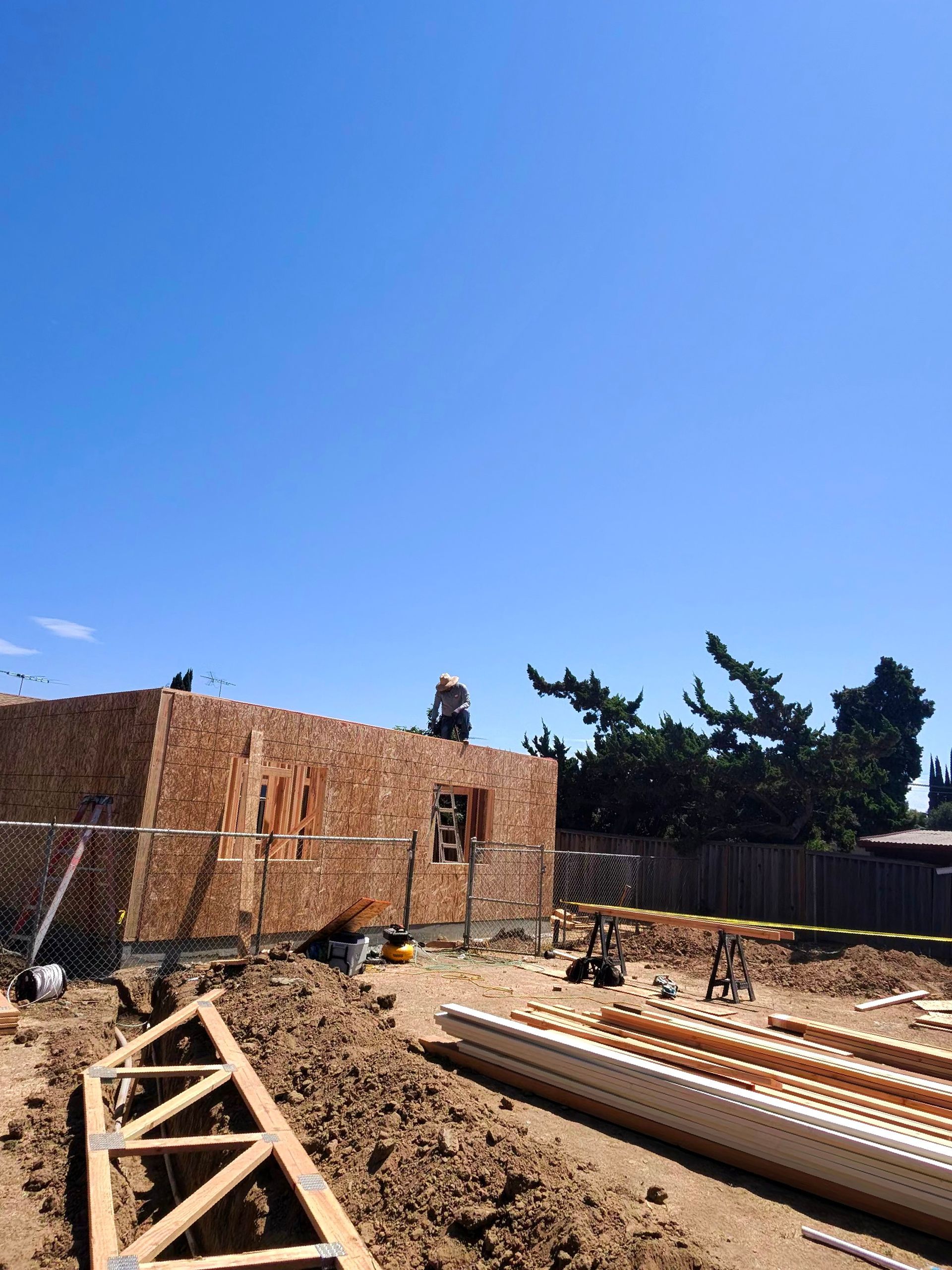 Construction site with brick wall, stacked lumber, and dirt under a clear blue sky