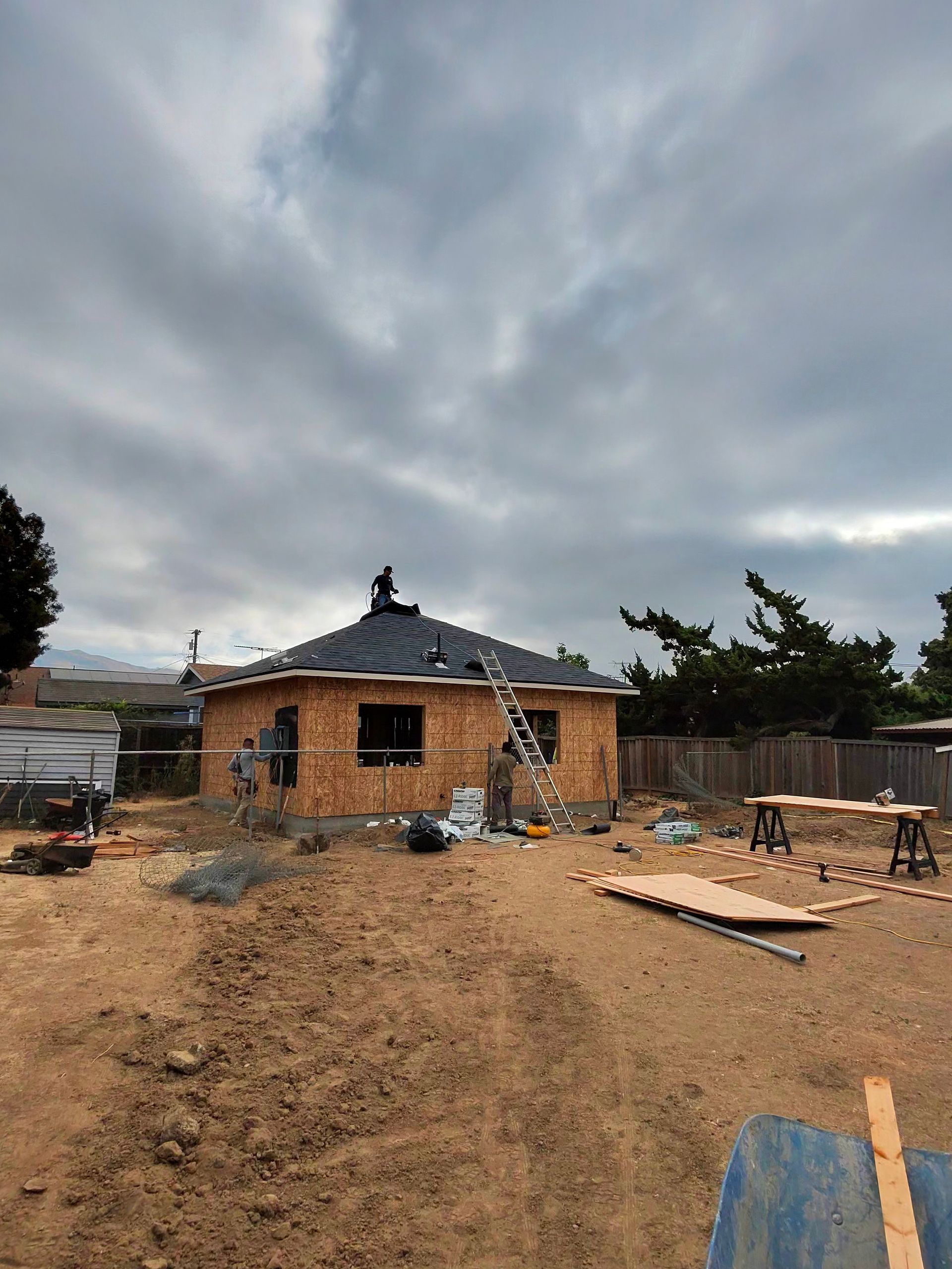 Partially built brick house under construction with scaffolding, wooden planks, and a cloudy sky