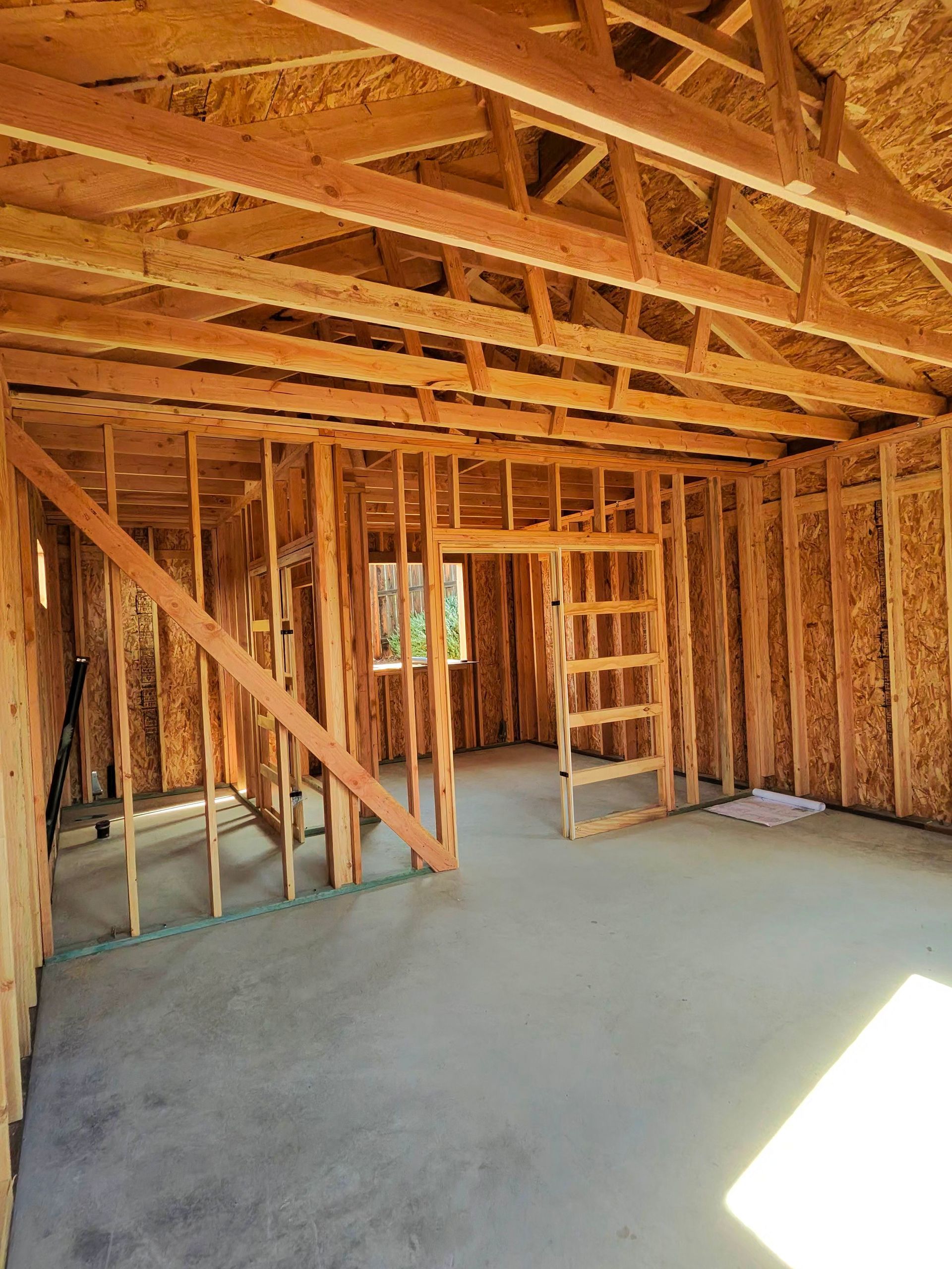 Unfinished wooden house interior with exposed framing, roof trusses, and a concrete floor