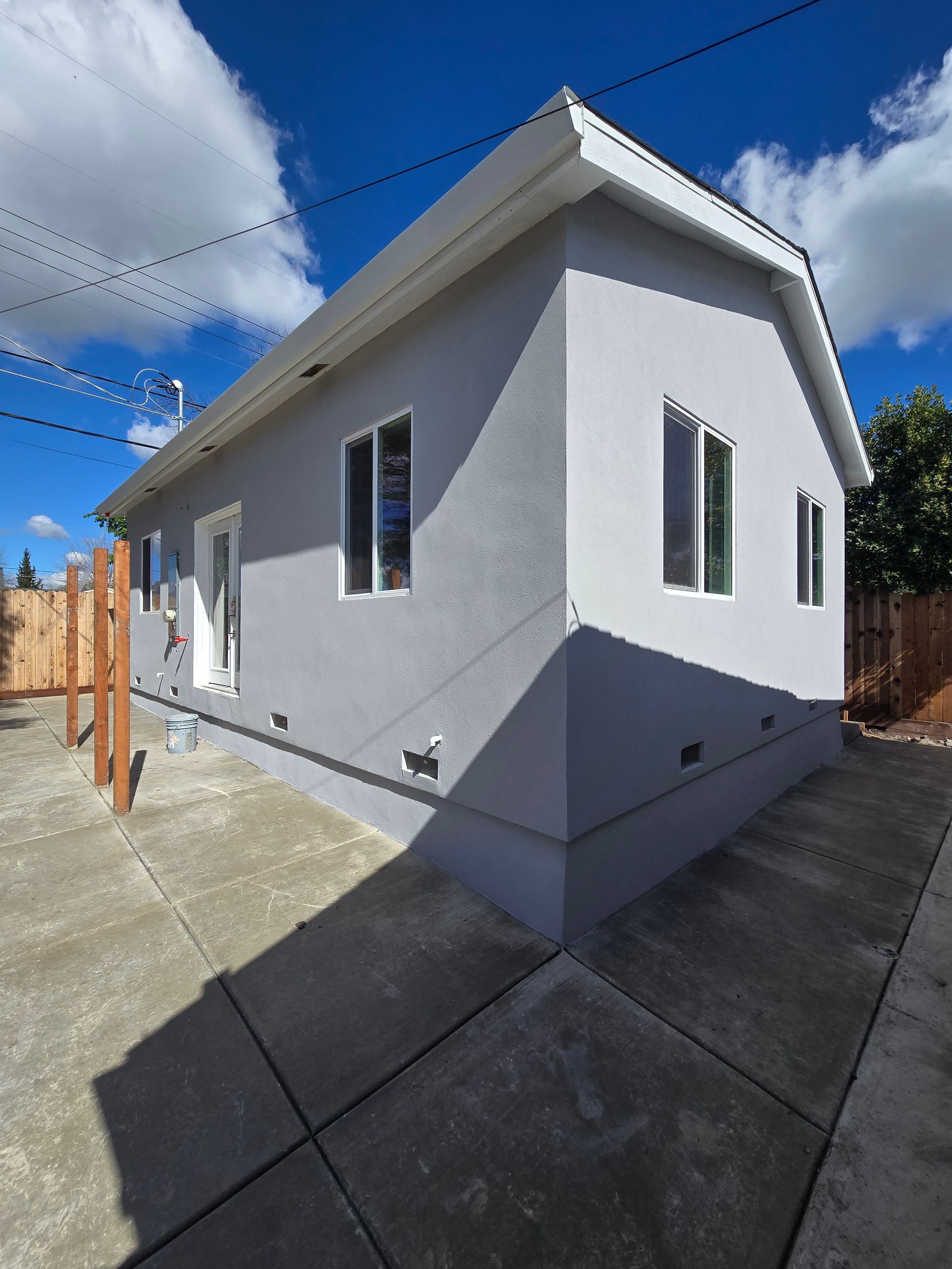 Small white house exterior with windows, concrete driveway, and blue sky on a sunny day