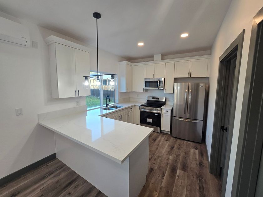 Bright modern kitchen with white cabinets, stainless steel appliances, and dark wood floors