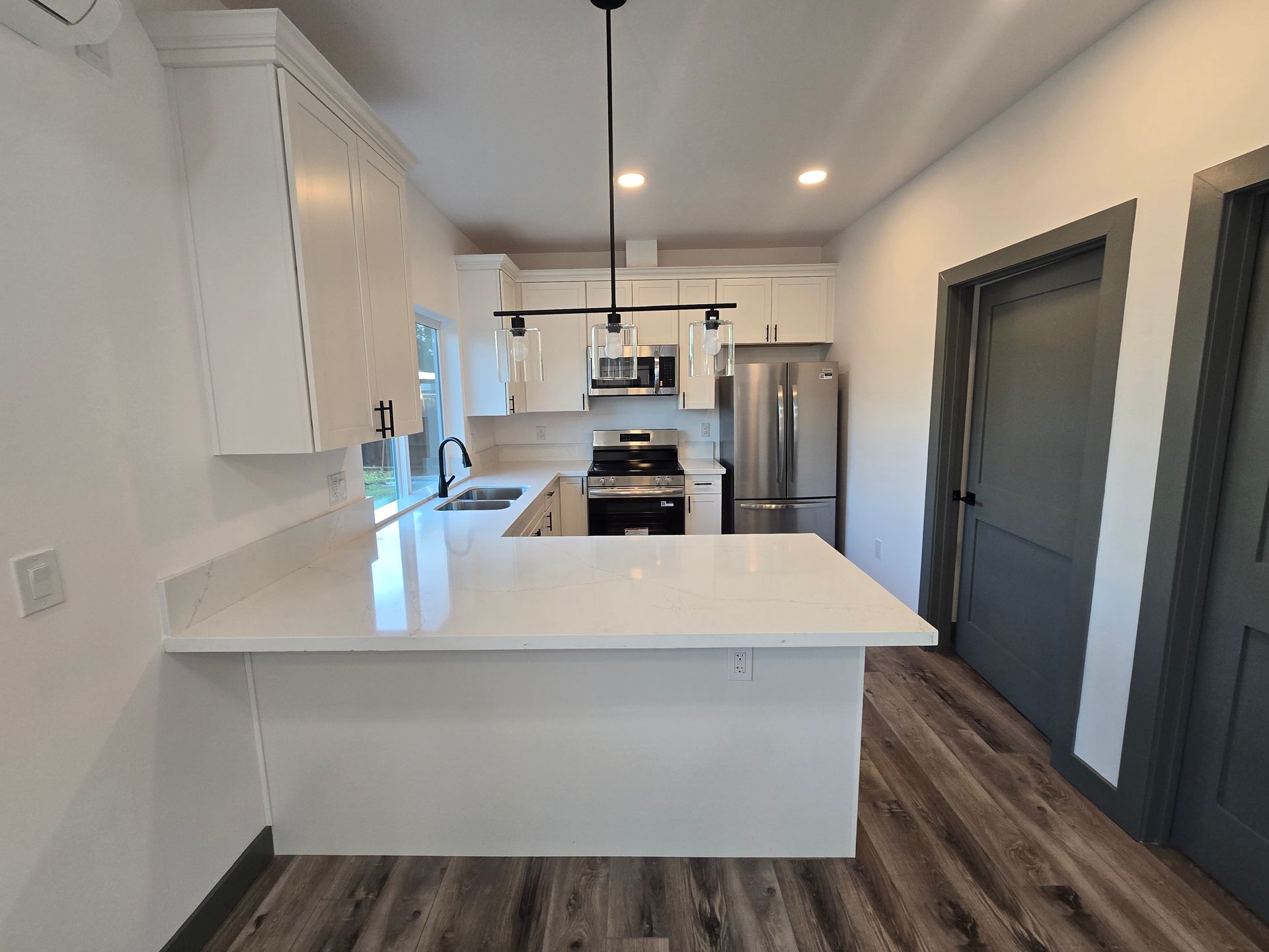 Modern kitchen with white island, stainless appliances, dark wood floor, and recessed lighting