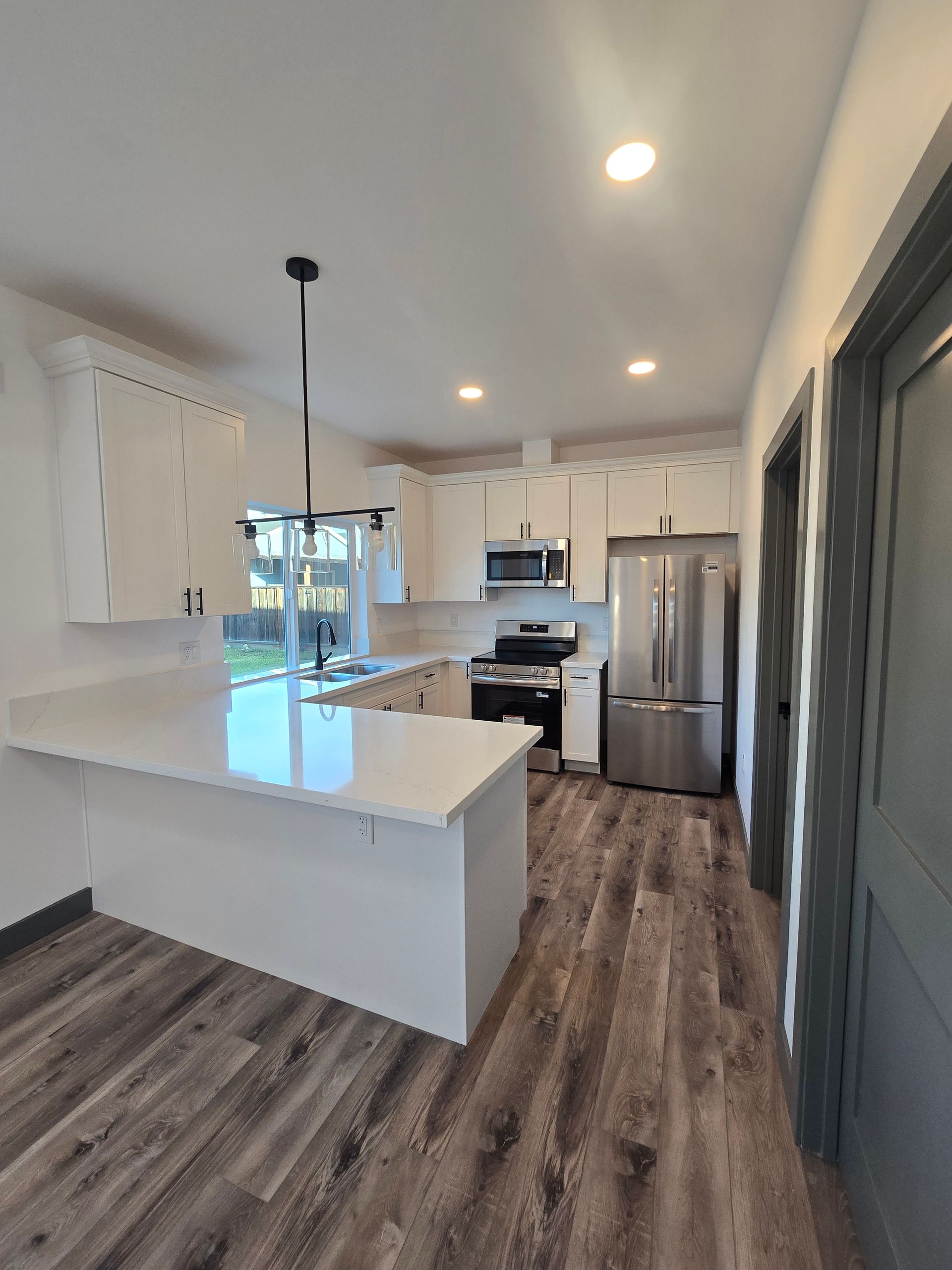 Modern kitchen with white cabinets, stainless steel appliances, island, and wood-look flooring.