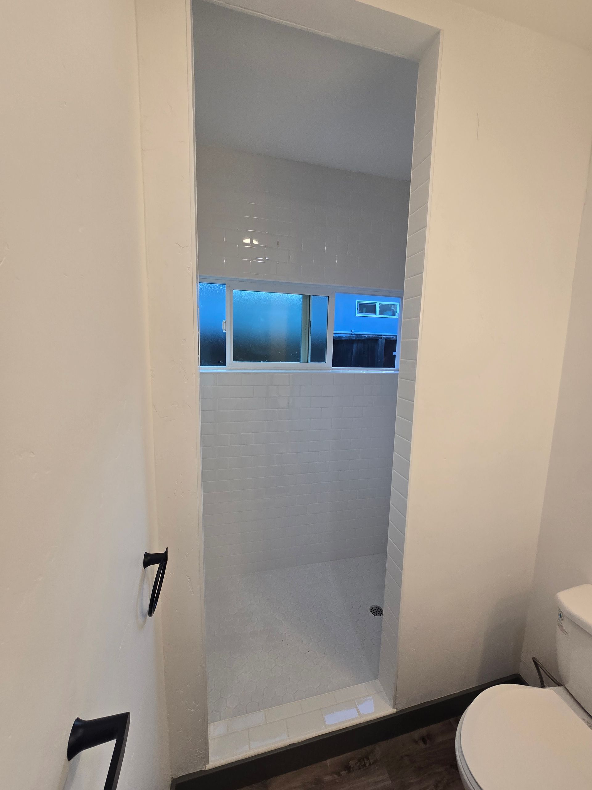 Small bathroom with a narrow shower alcove, white tile, and a window ledge above the shower.